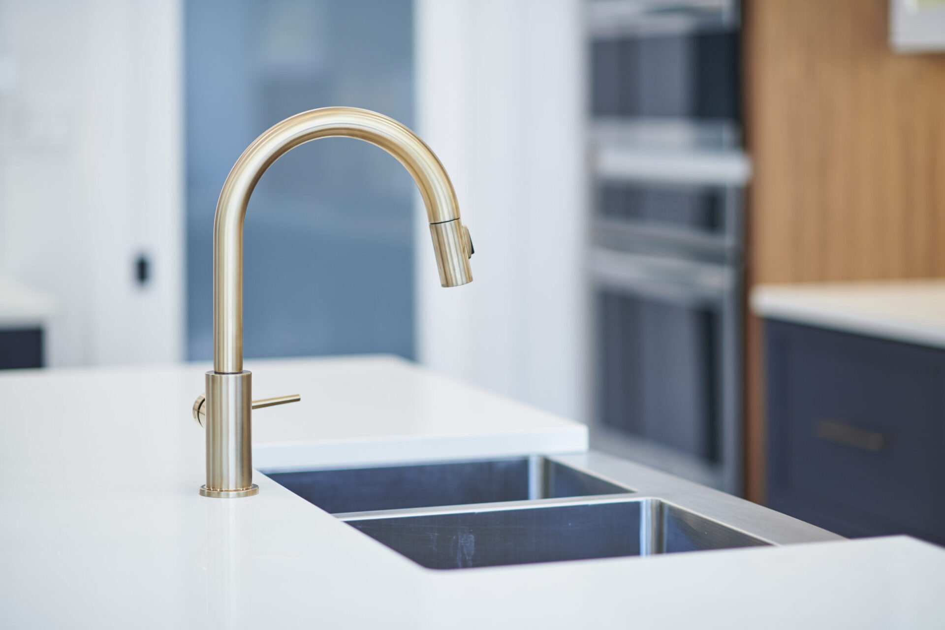 A modern kitchen with a gold-toned faucet and double sink, white countertop, and blue cabinetry blurred in the background. Stylish and clean interior.