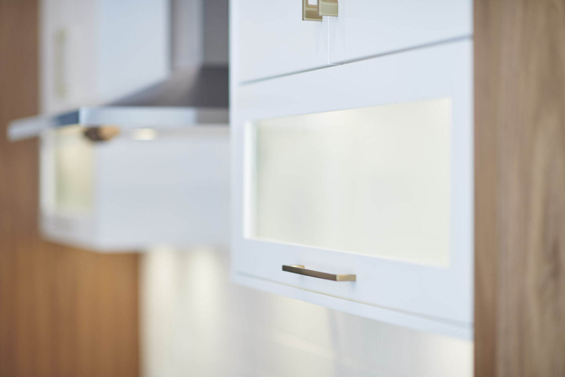 A modern kitchen detail emphasizing clean lines, with a white cupboard featuring a frosted glass panel and minimalistic metal handle.