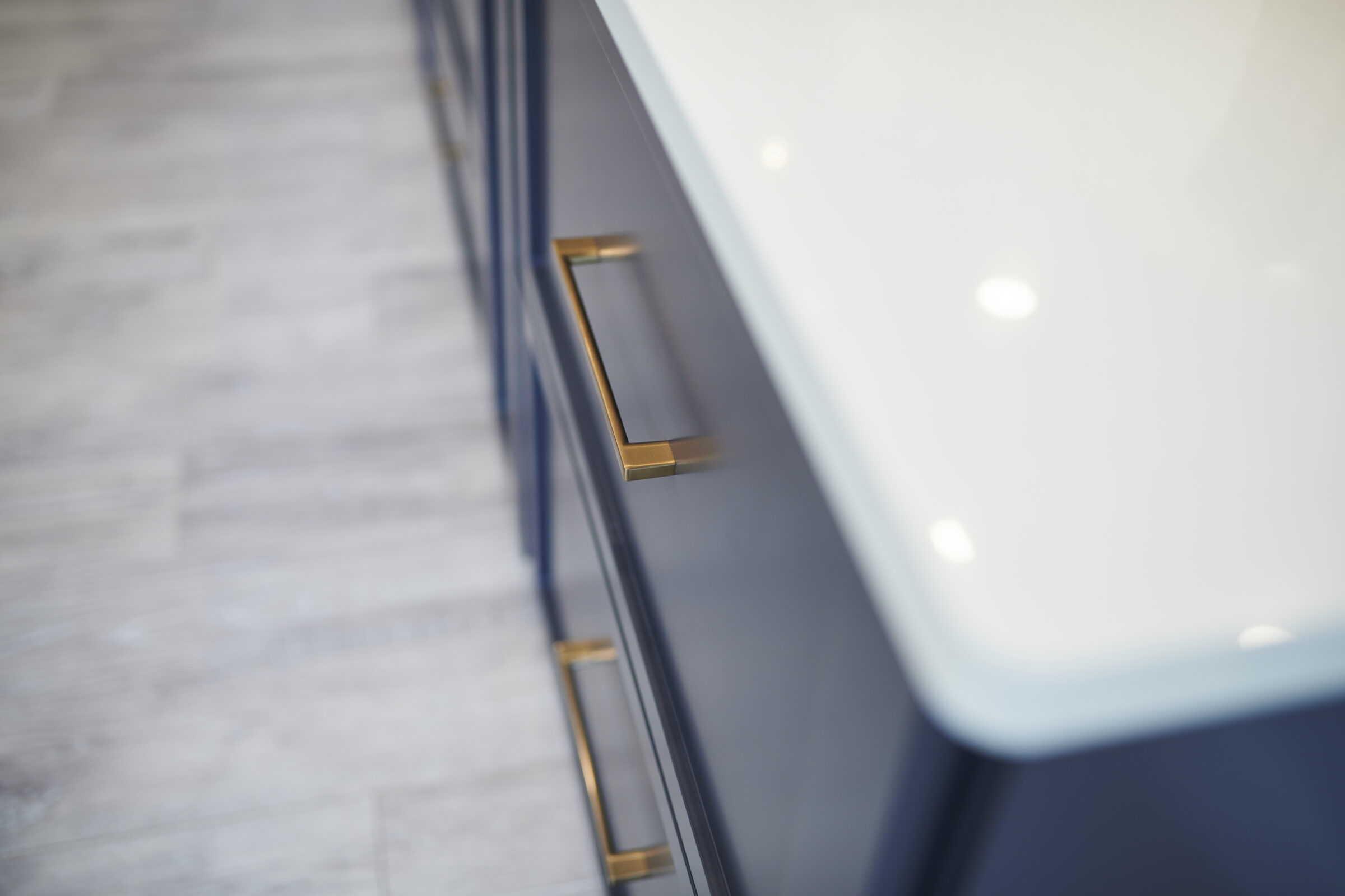 A modern kitchen cabinet with sleek blue-gray doors and elegant gold handles. Against a backdrop of light wood flooring, the clean, minimalist design stands out.