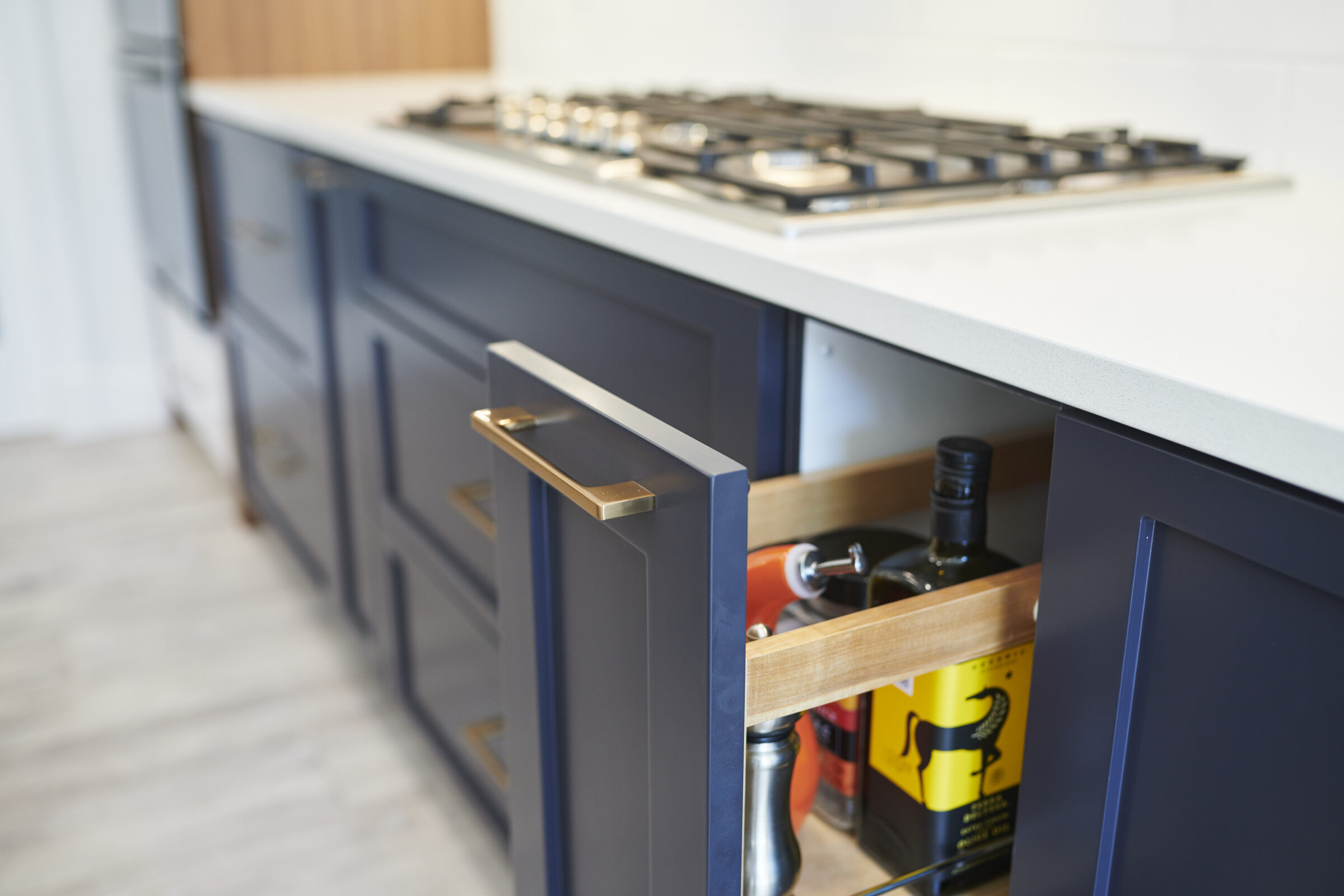 Modern kitchen with blue cabinets, a white countertop, and a gas stove. An open cabinet reveals bottles and a wine rack inside.