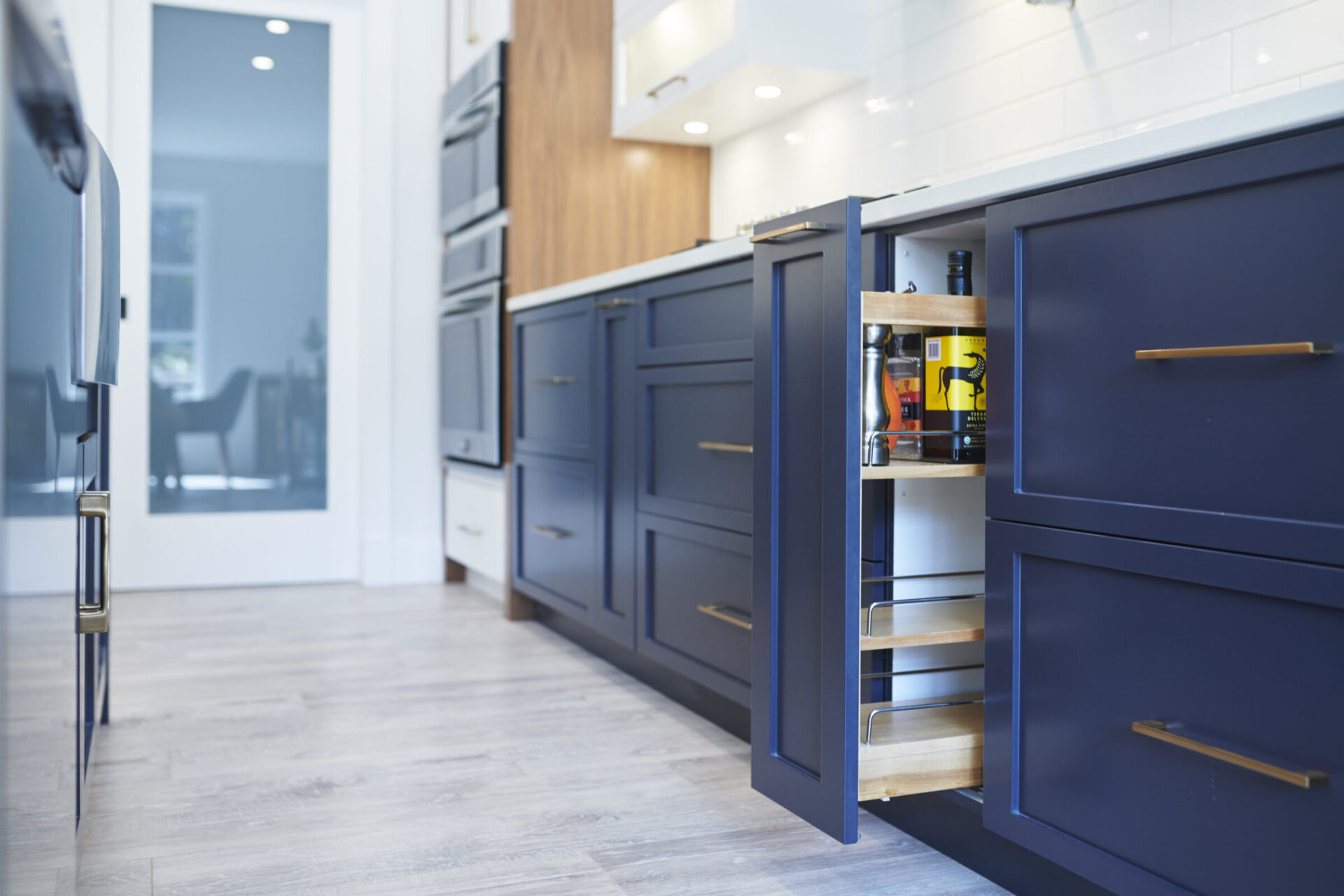 Modern kitchen with sleek blue cabinets and a pull-out spice rack. Stainless steel appliances and light wood flooring complement the clean design.