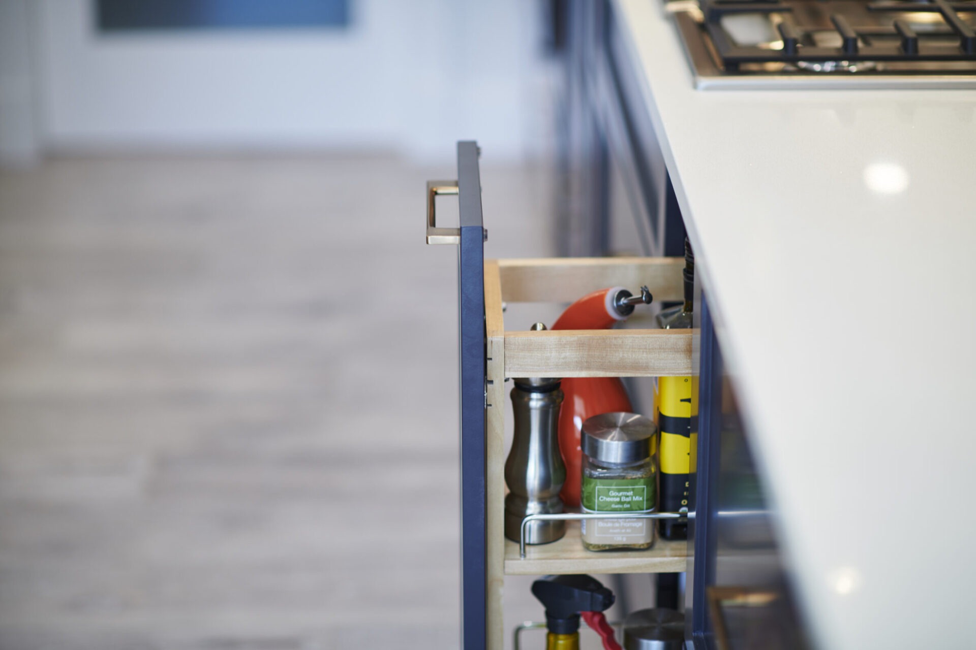 A modern kitchen drawer is partially open, revealing organized storage with spices, a pepper grinder, and cooking utensils within a wooden compartment.