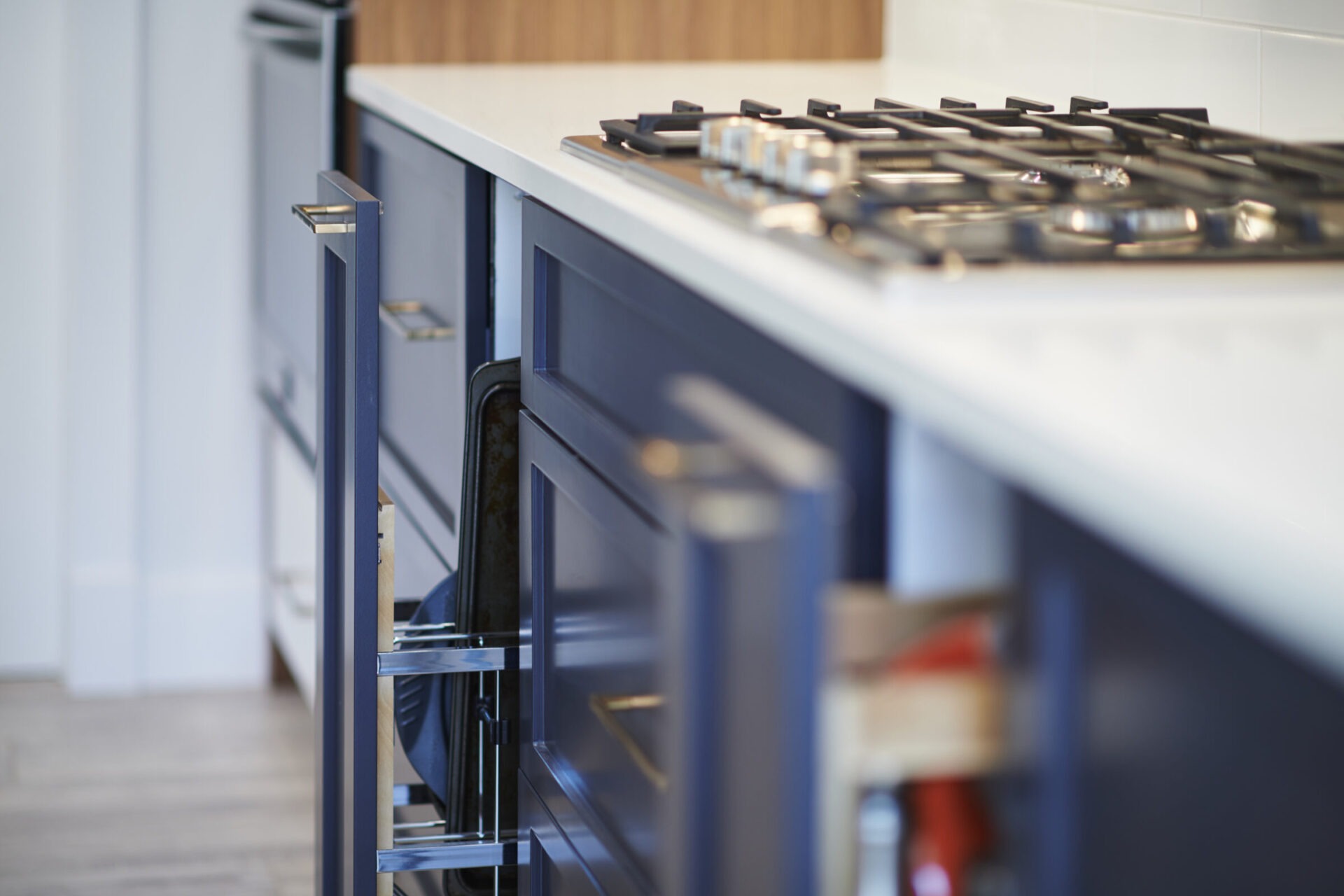 A modern kitchen with blue cabinets, stainless steel handles, a white countertop, and a gas cooktop with black burners. Focus is on the cabinetry.