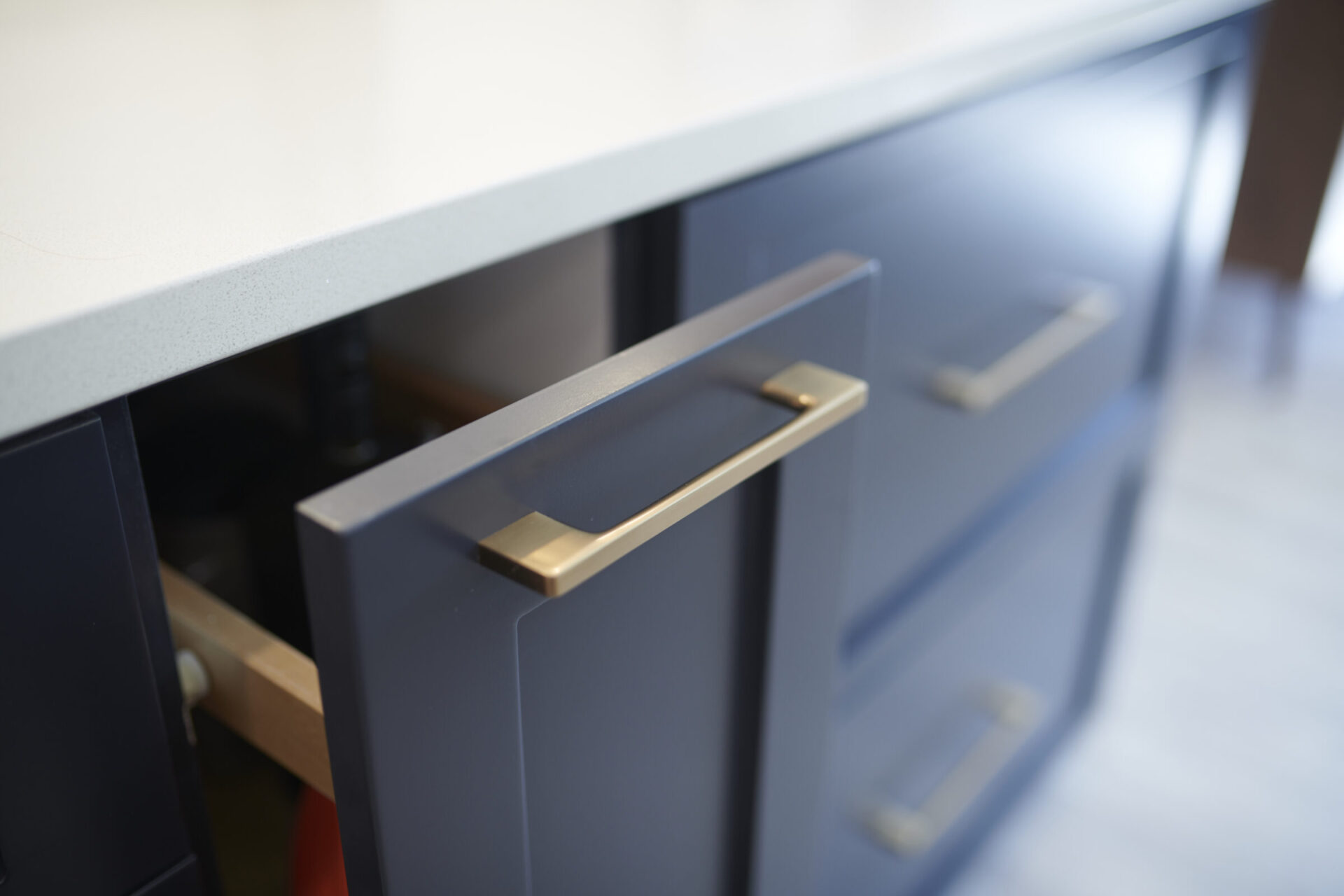 A close-up image showing a modern blue cabinet with a partially opened drawer, featuring sleek golden handles, against a white countertop.