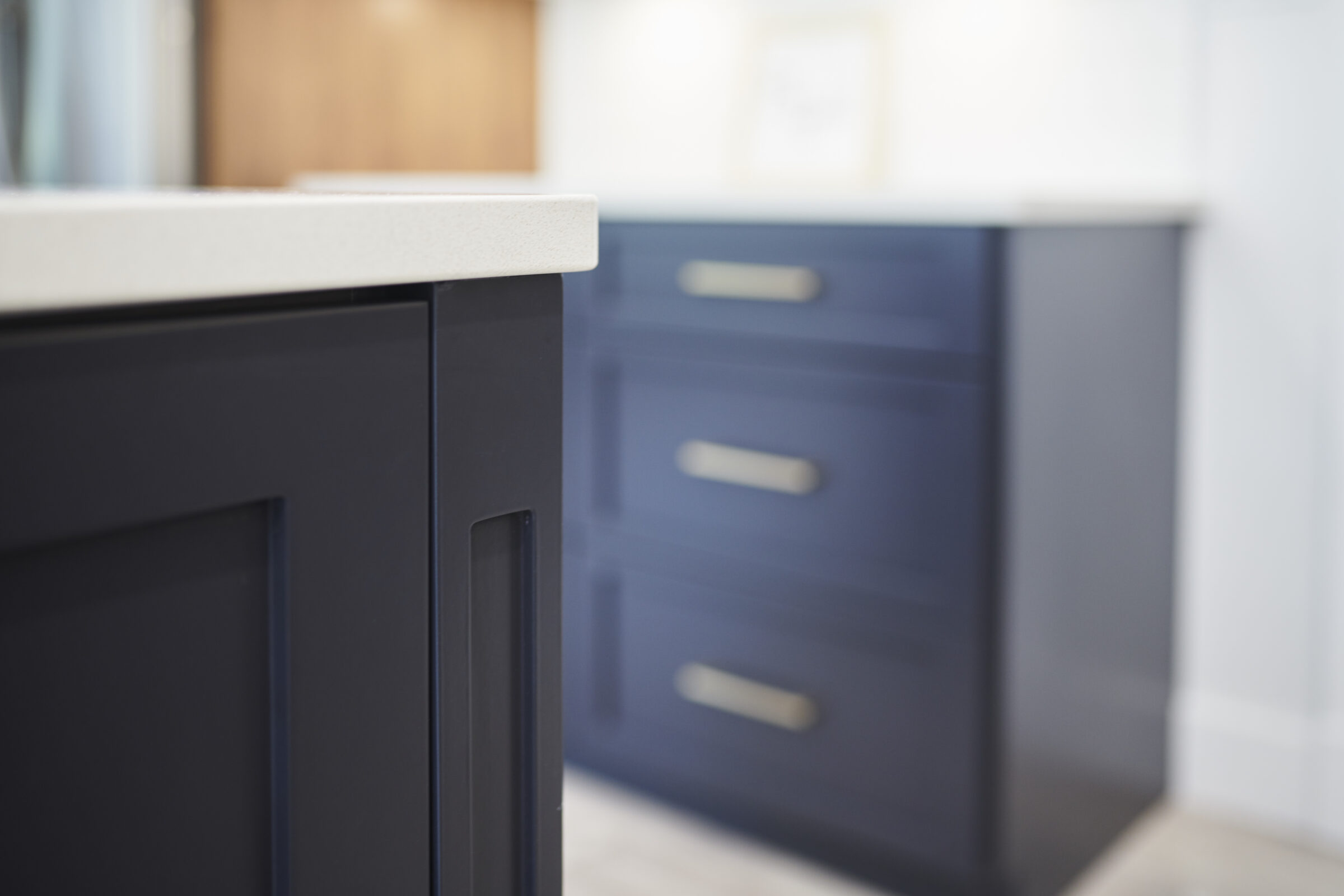 The image shows a close-up of a kitchen's corner with a focus on the cabinetry, featuring a navy blue island with silver handles, out of focus.