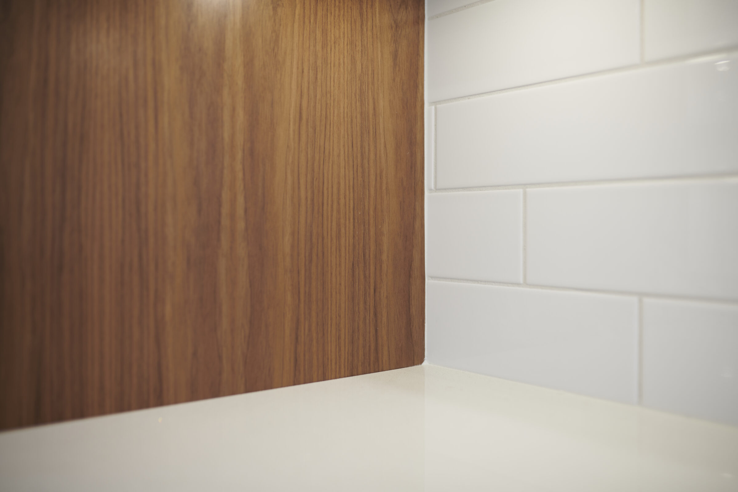 This image shows a close-up of a kitchen corner with wood and white tile textures meeting on a light countertop, illustrating clean interior design elements.