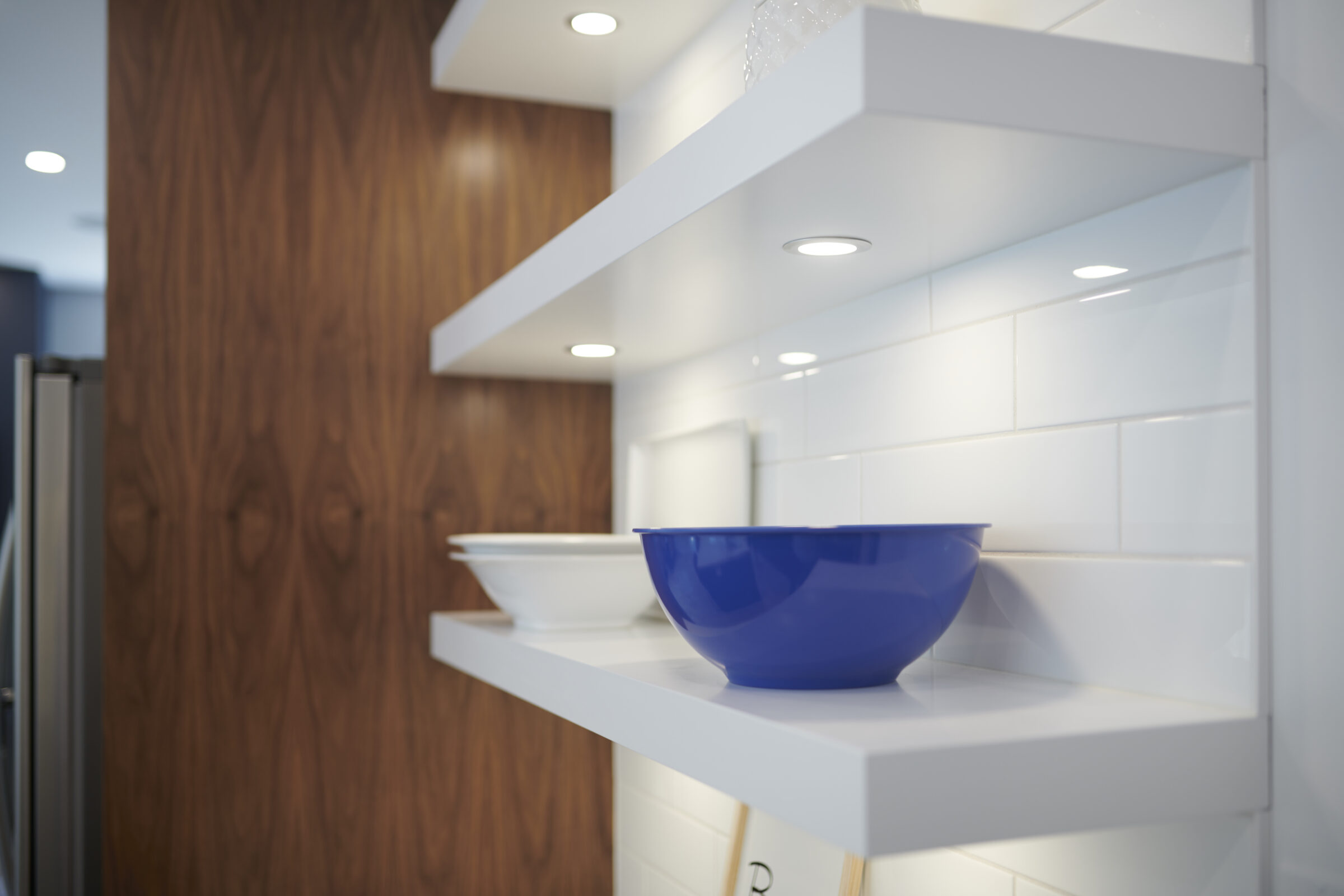 Modern kitchen with white floating shelves on a subway-tiled wall, featuring a vibrant blue bowl as a focal point, set against a warm wooden backdrop.