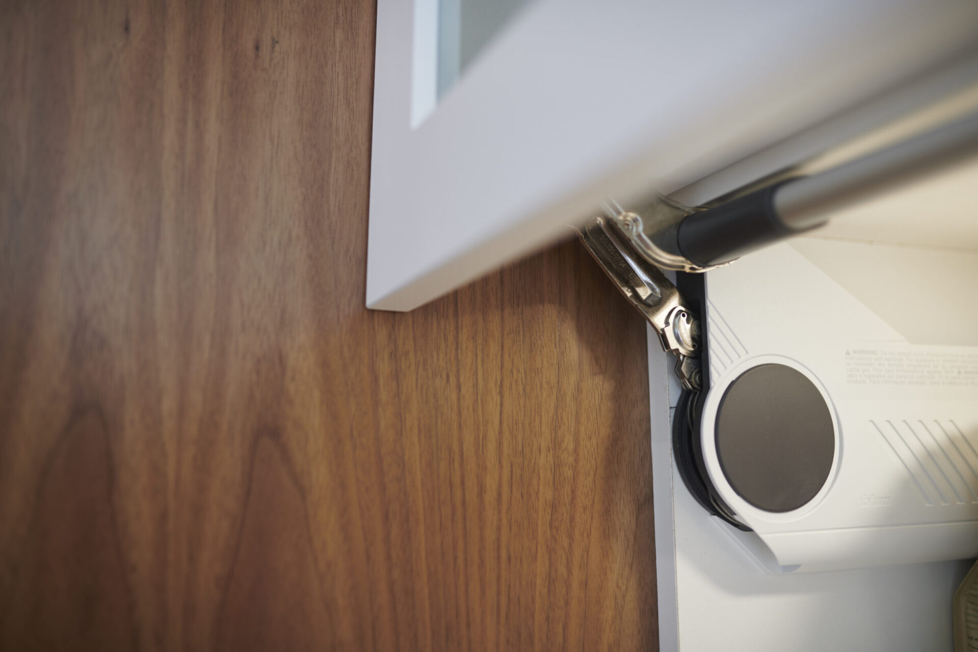 An open book rests beneath a desk lamp near a white device, on a surface with wood grain, showcasing a focused, close-up perspective.