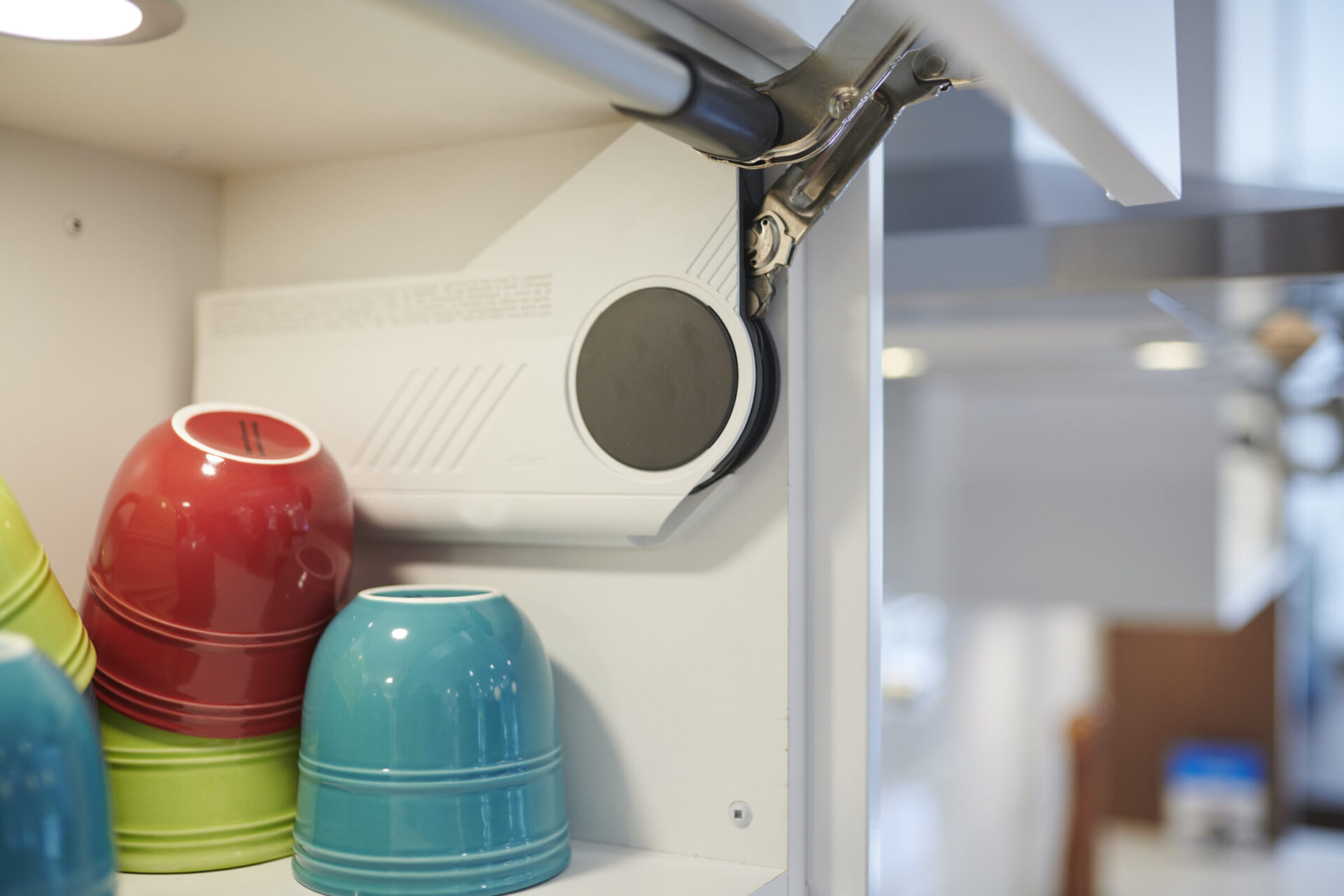 A focused image of colorful ceramic pots on a shelf, with a blurred background of a projector mounted on a white ceiling.