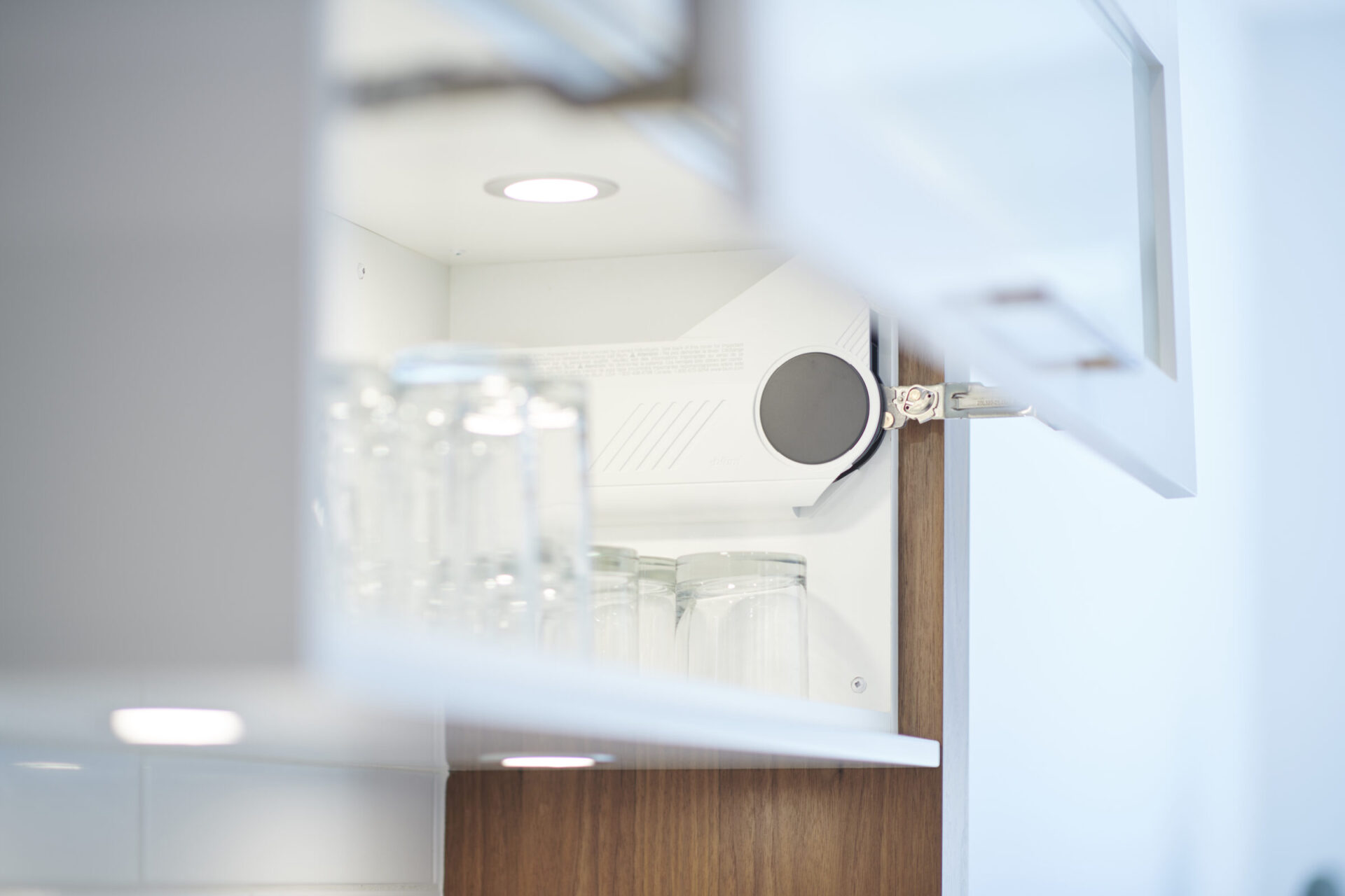 The image shows a blurred kitchen cabinet with an open door, revealing a shelf with glassware, hinting at a clean and orderly space.