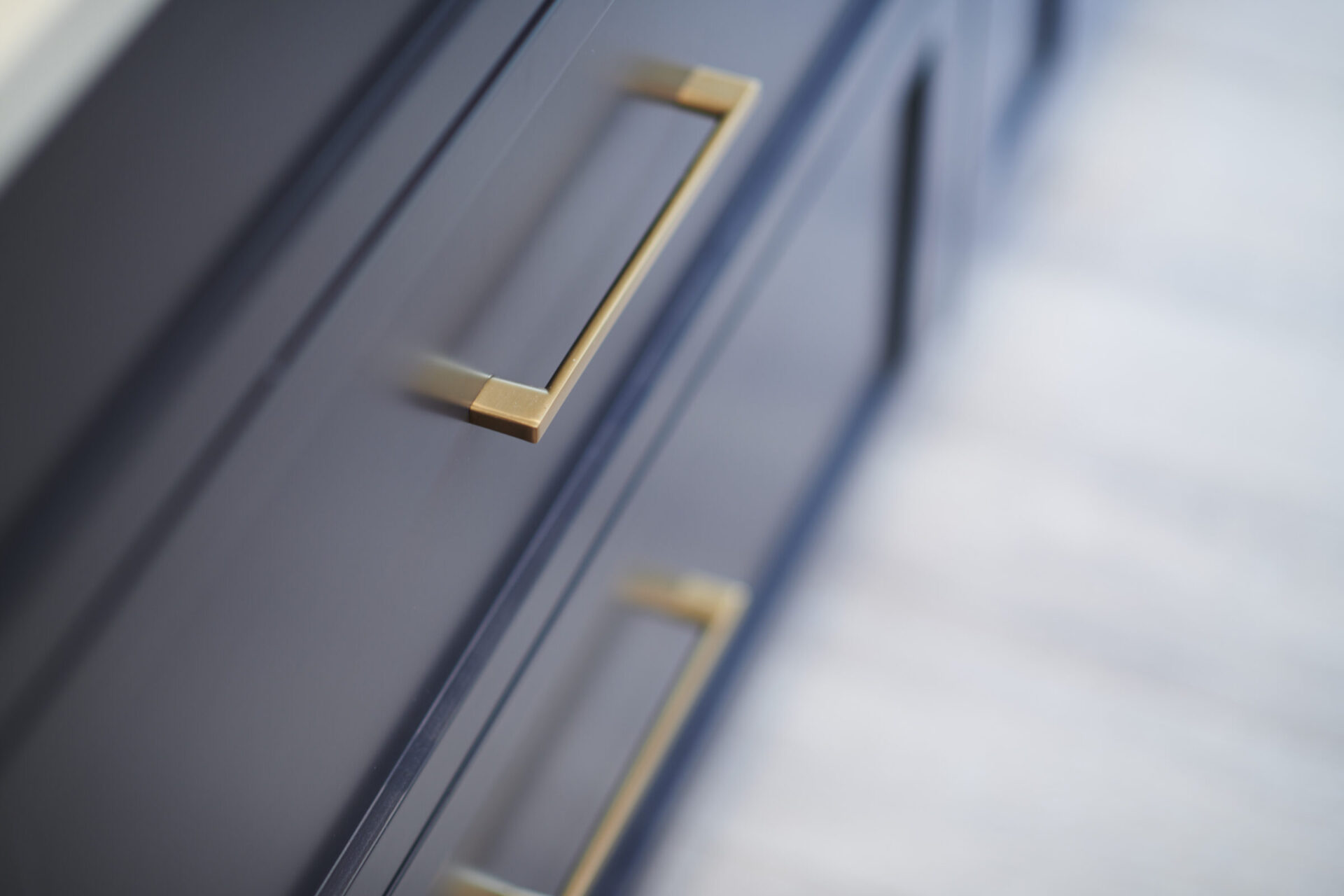 This image shows a close-up of a navy blue cabinet with sleek gold handles, featuring clean lines and a modern aesthetic with soft-focus background.