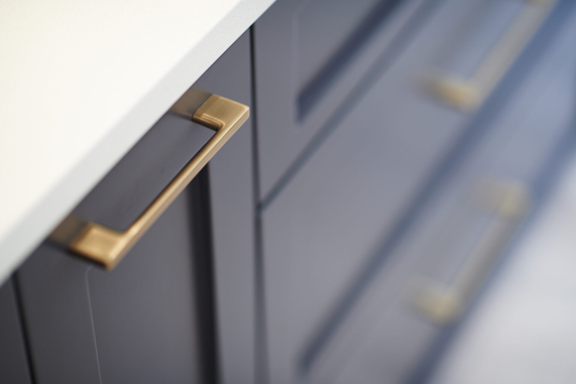 Close-up of a gray cabinet with a metallic gold handle, with a blurred background emphasizing the detail and texture of the furniture.