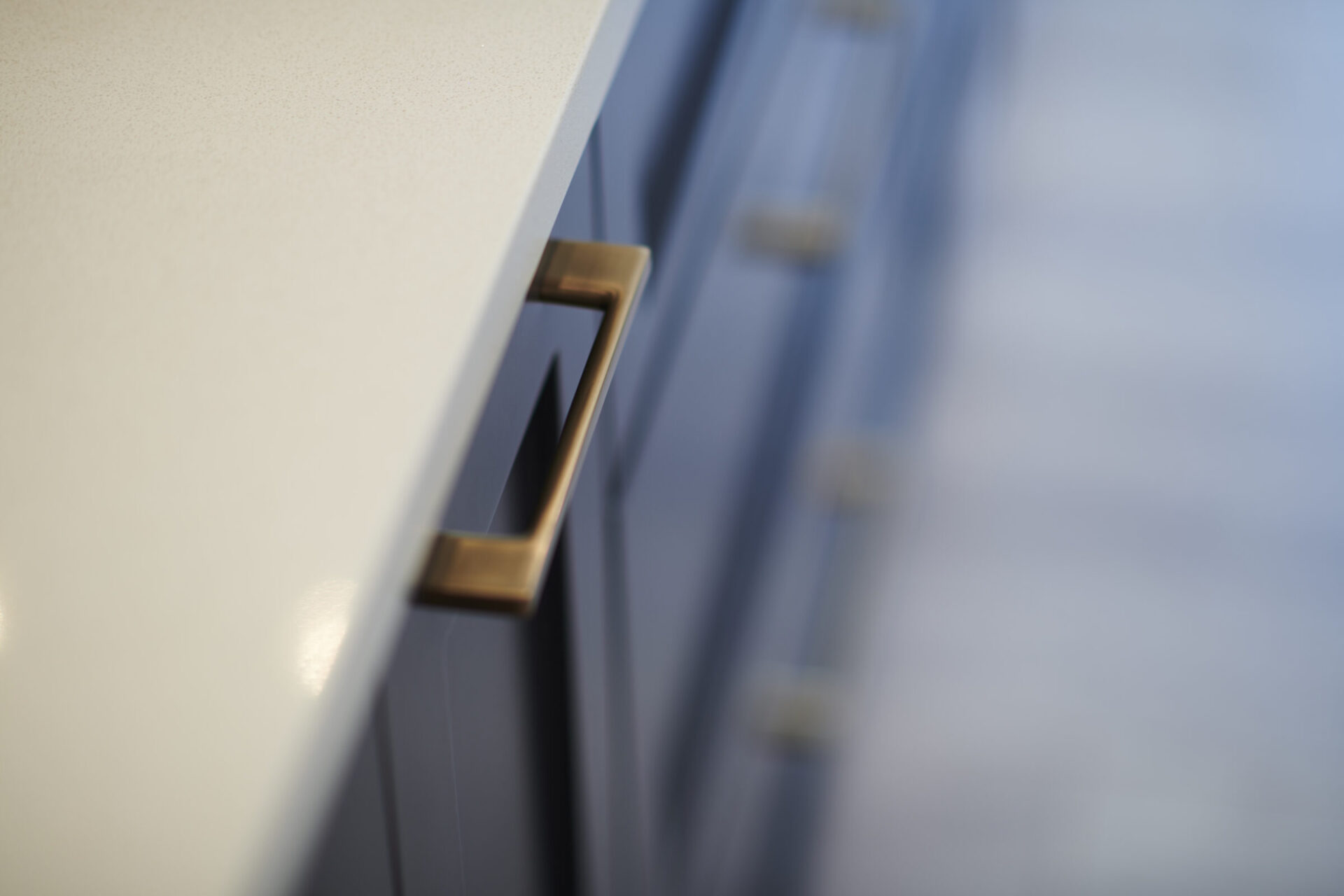 A close-up image of a counter edge with a blurred background, focusing on a dark drawer with a rectangular bronze handle.