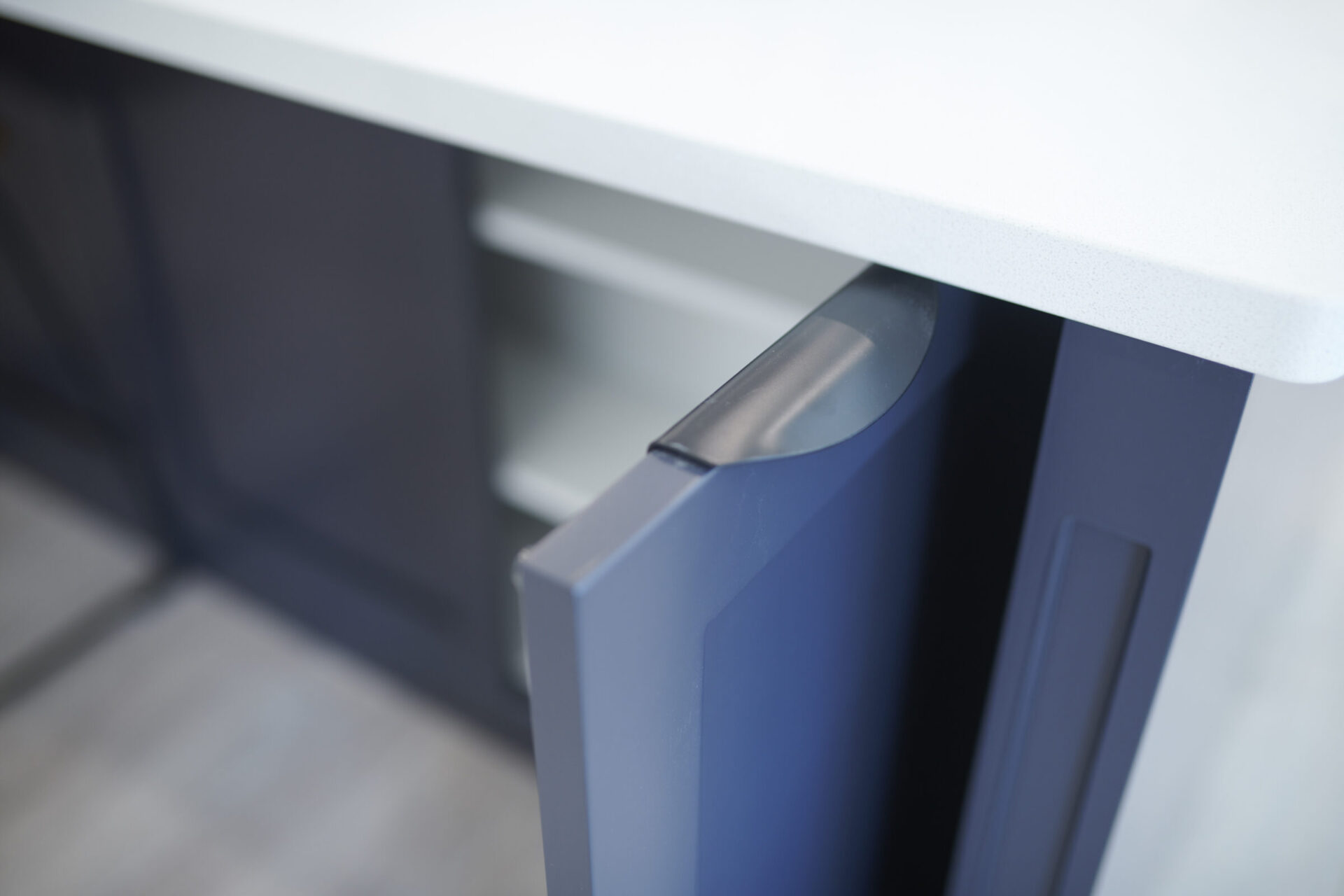 A close-up image of a modern desk's edge, showcasing a white tabletop and a sleek blue support with a minimalist design.