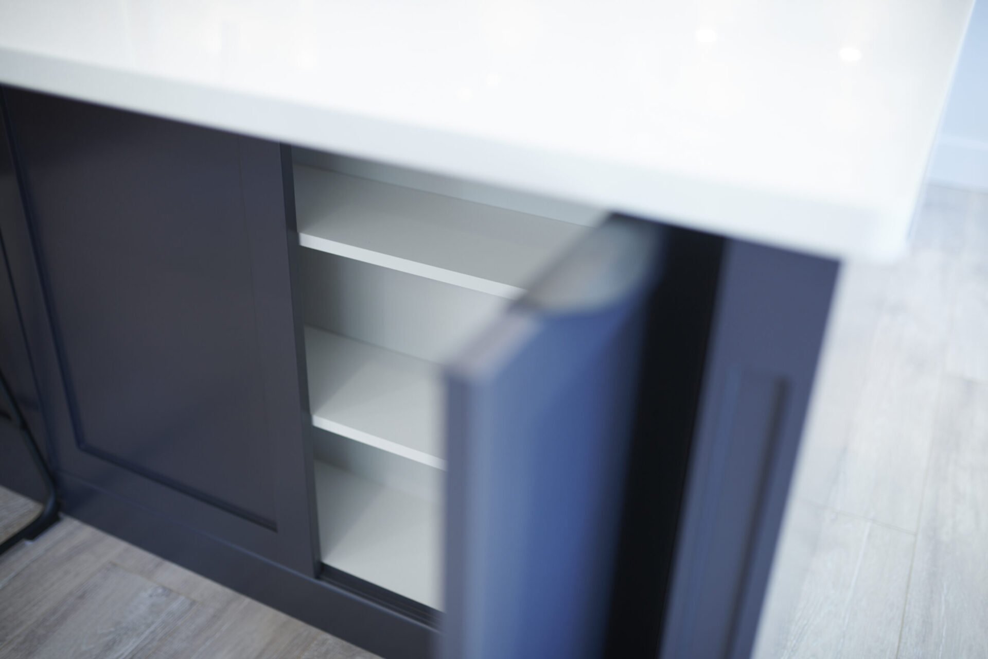 This image shows a modern kitchen cabinet with an open door, revealing empty white shelves within. The overall setting has a clean and sleek design.