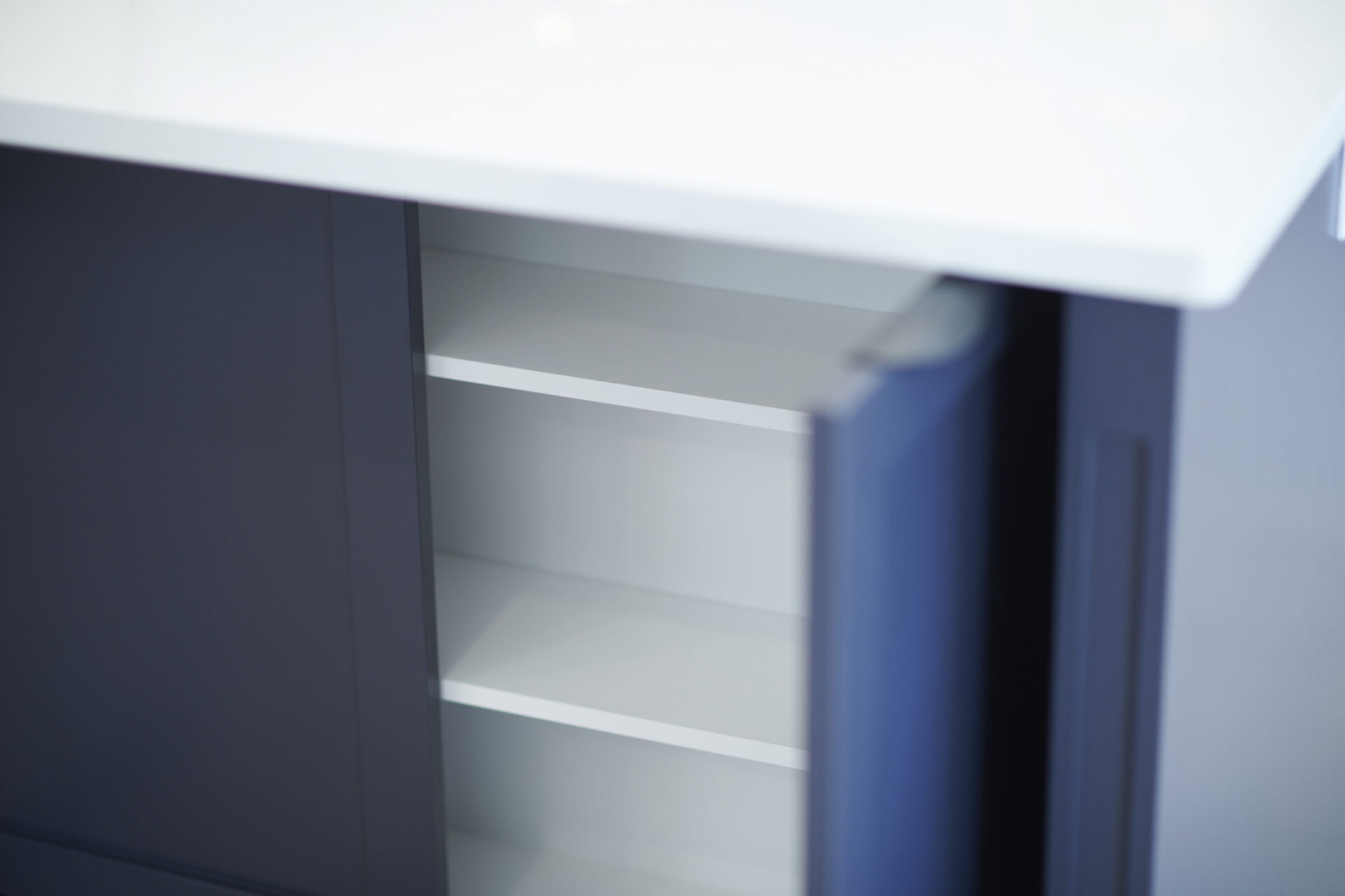 The image shows a close-up of a modern, empty cabinet with white shelves, partially obscured by an open blue door, with a blurred background.