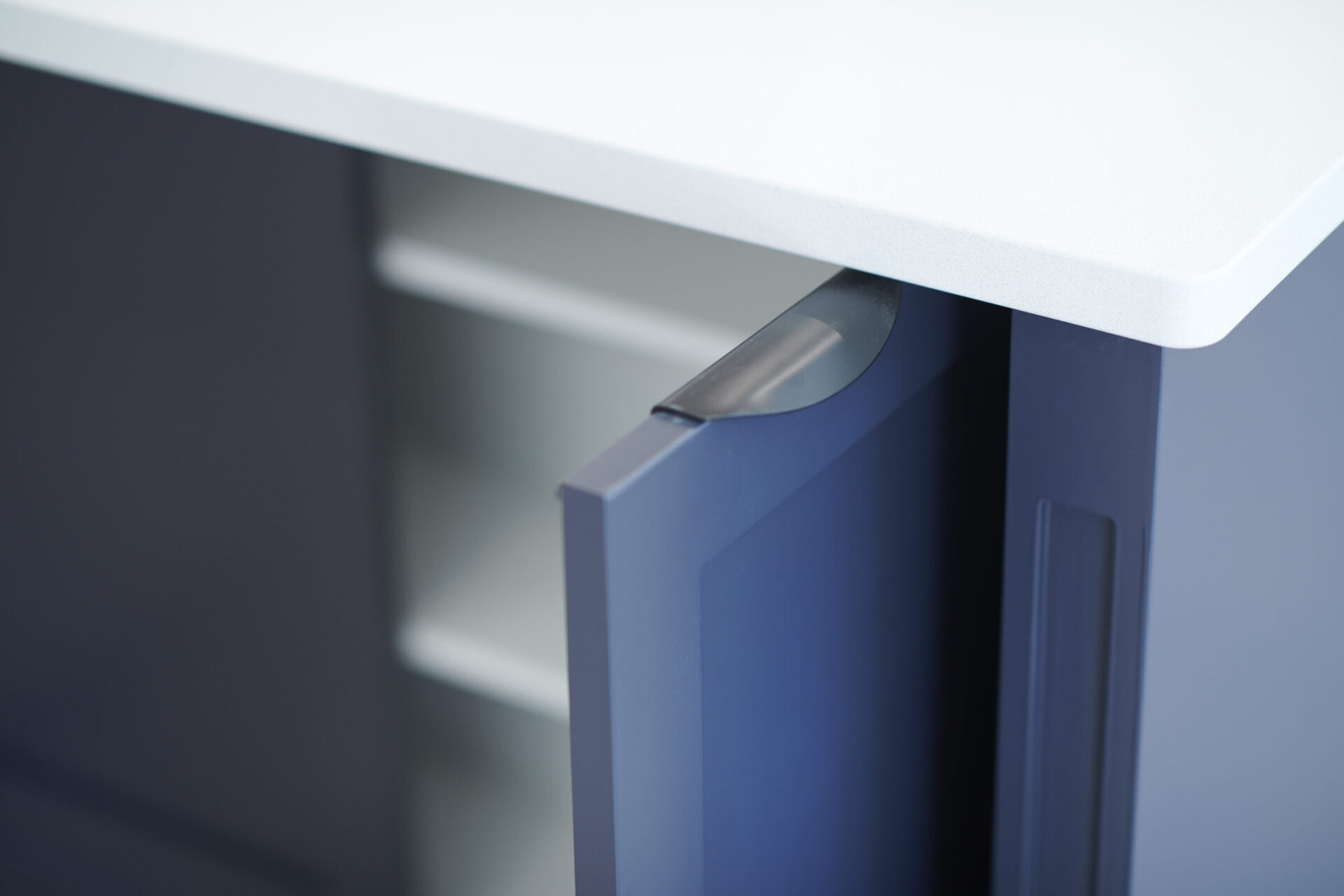 Close-up of a modern desk with a white tabletop and blue supports, focusing on the edge where a metallic cable management feature is visible.