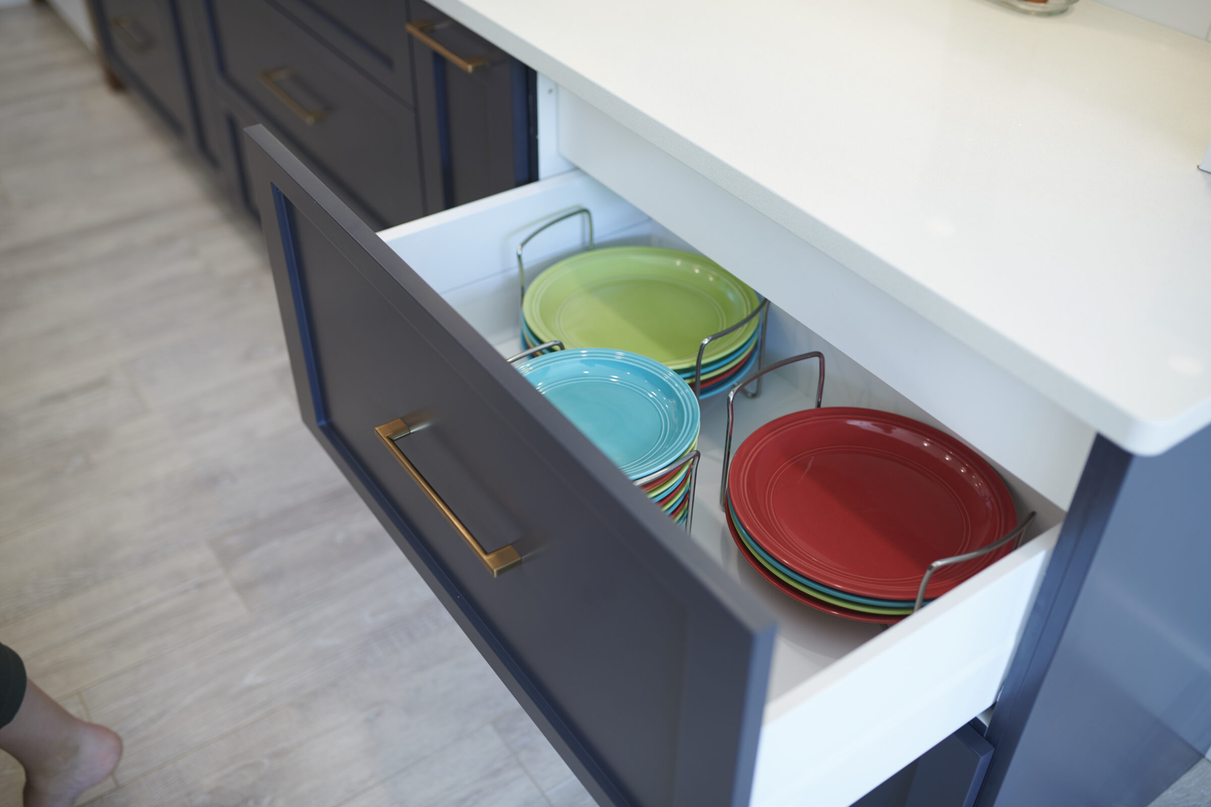 A kitchen drawer is open, revealing neatly stacked colorful plates. The modern cabinetry has a sleek design with a gold handle.