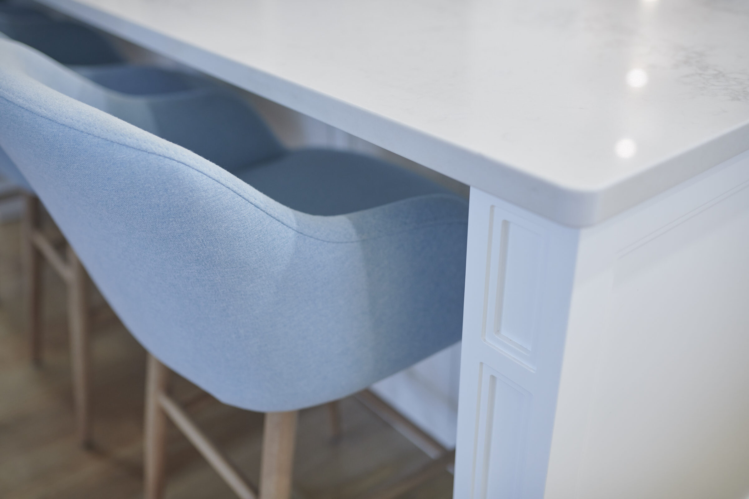 This image shows a white marble countertop with a white cabinet base and a row of blue upholstered bar stools with wooden legs.