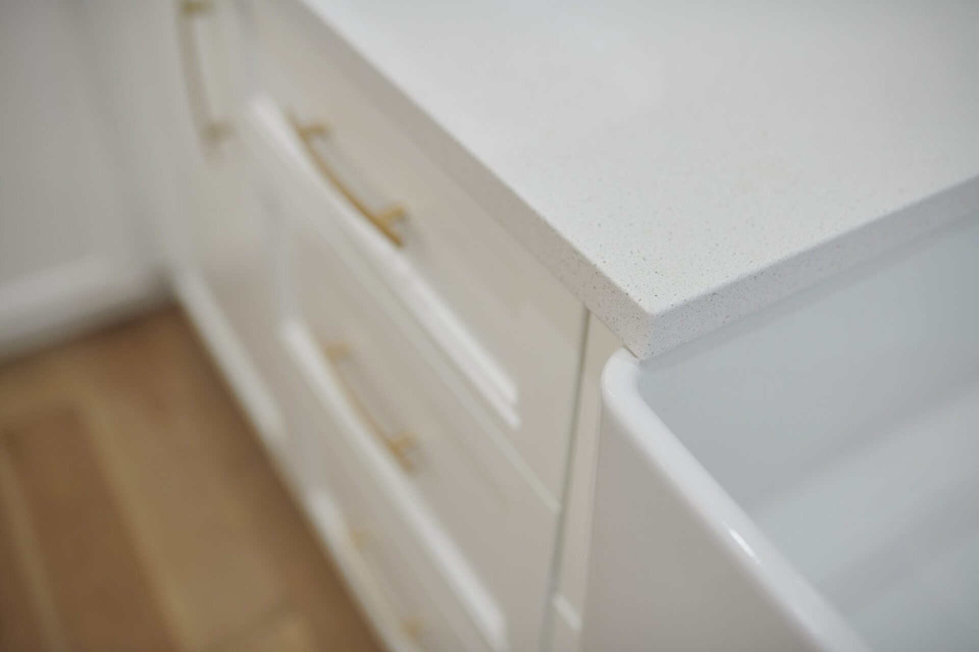 This image shows a close-up of a white kitchen countertop with speckled pattern, above white cabinets with gold handles, against a soft-focus background.