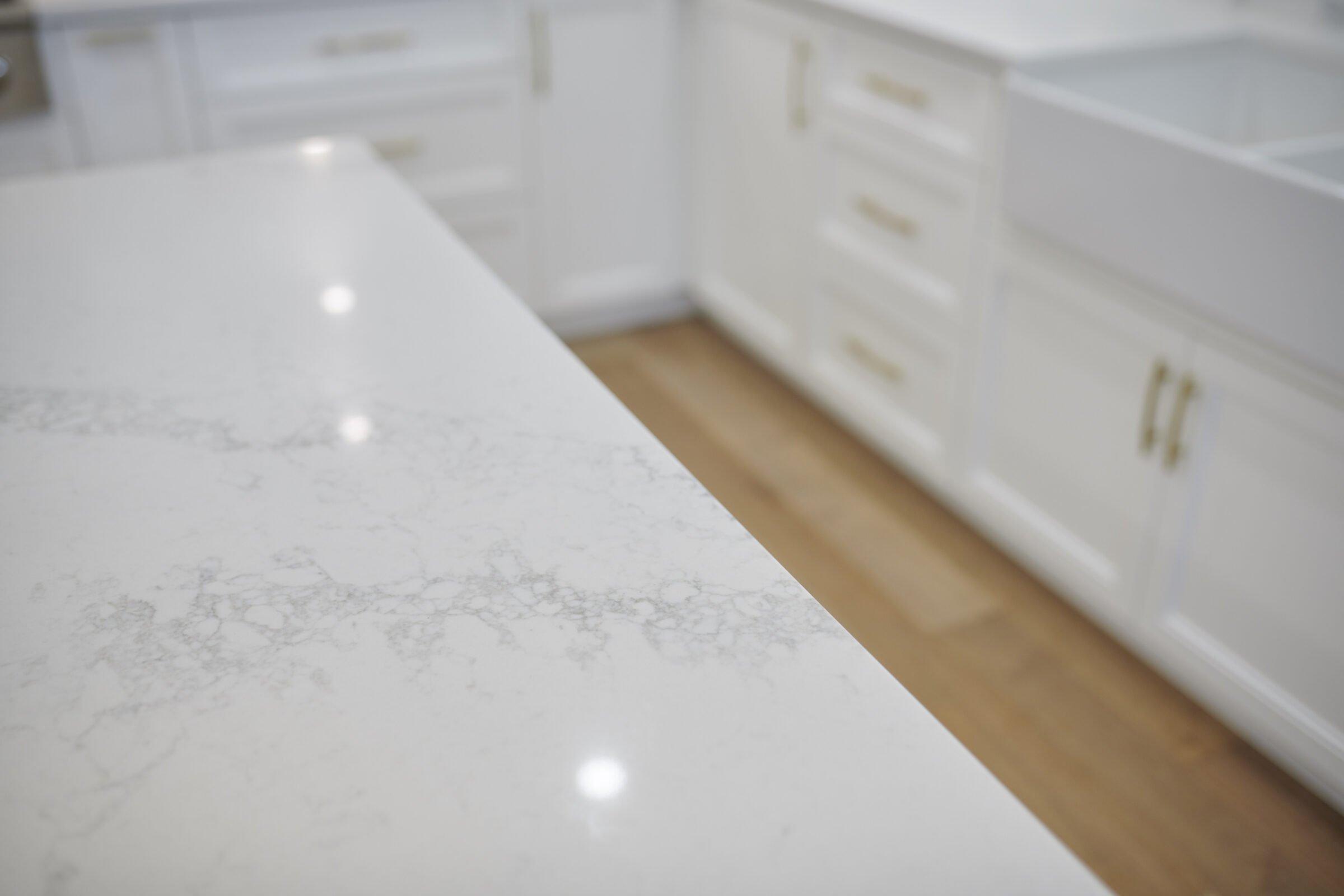 A modern kitchen showcasing a pristine white marble countertop with subtle gray veins, complemented by white cabinetry and gold handles.