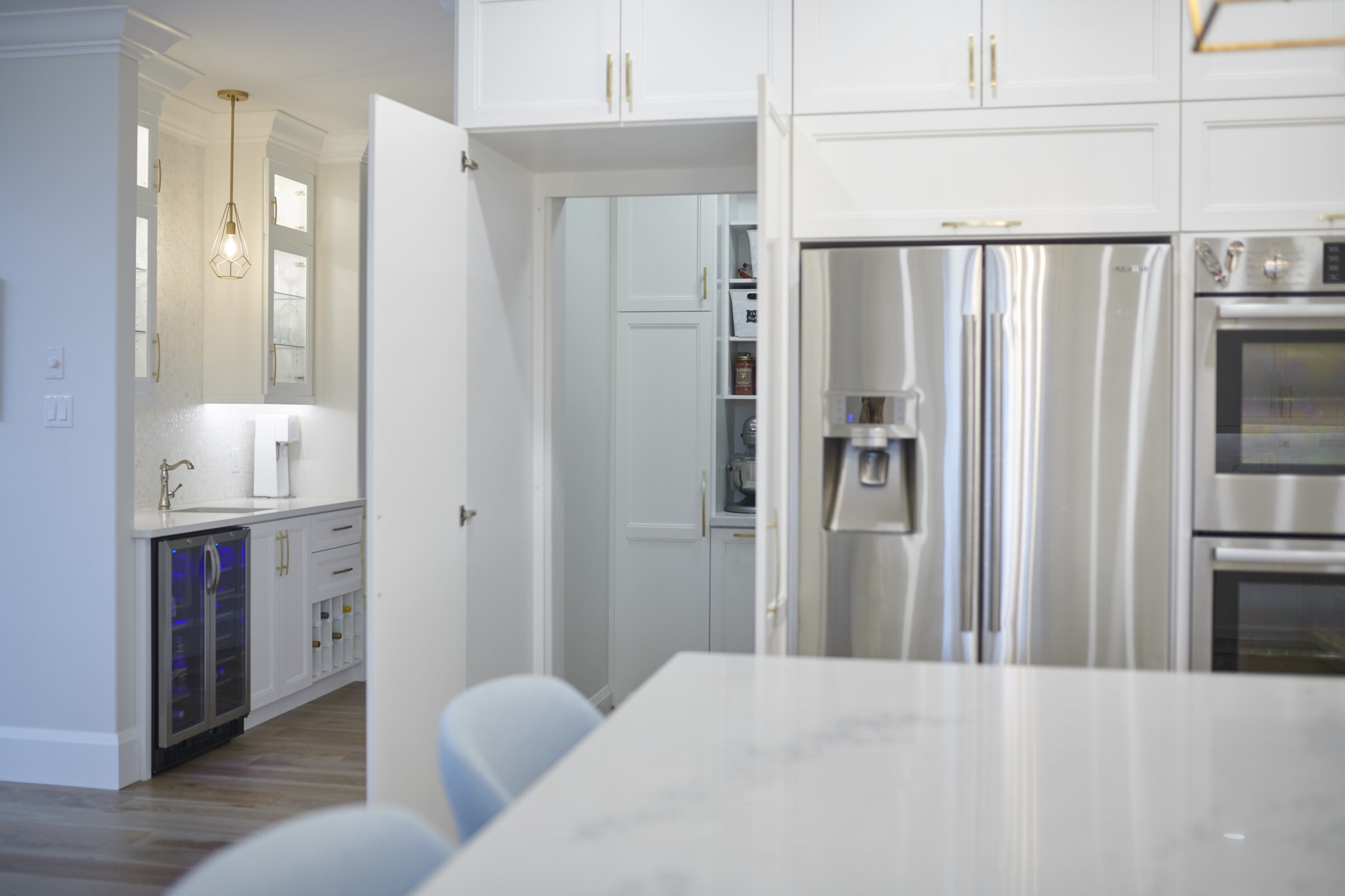 This image shows a modern kitchen with white cabinetry, stainless steel appliances, a wine cooler, and marble countertops, in a clean, bright interior.