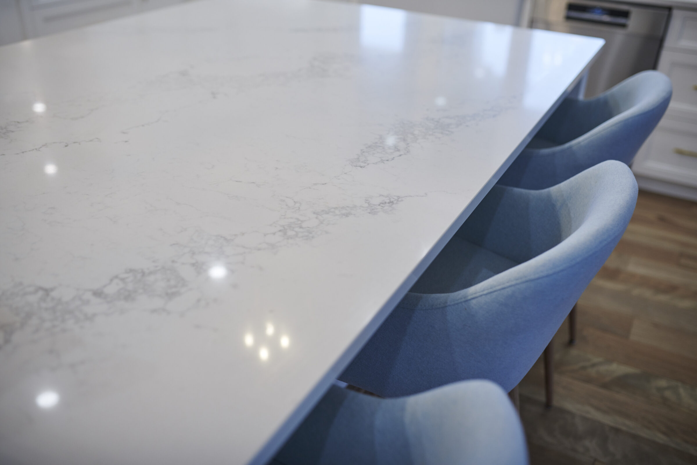 A modern kitchen with a white marble countertop island and blue upholstered chairs reflecting a gleaming, clean, and minimalist design aesthetic.