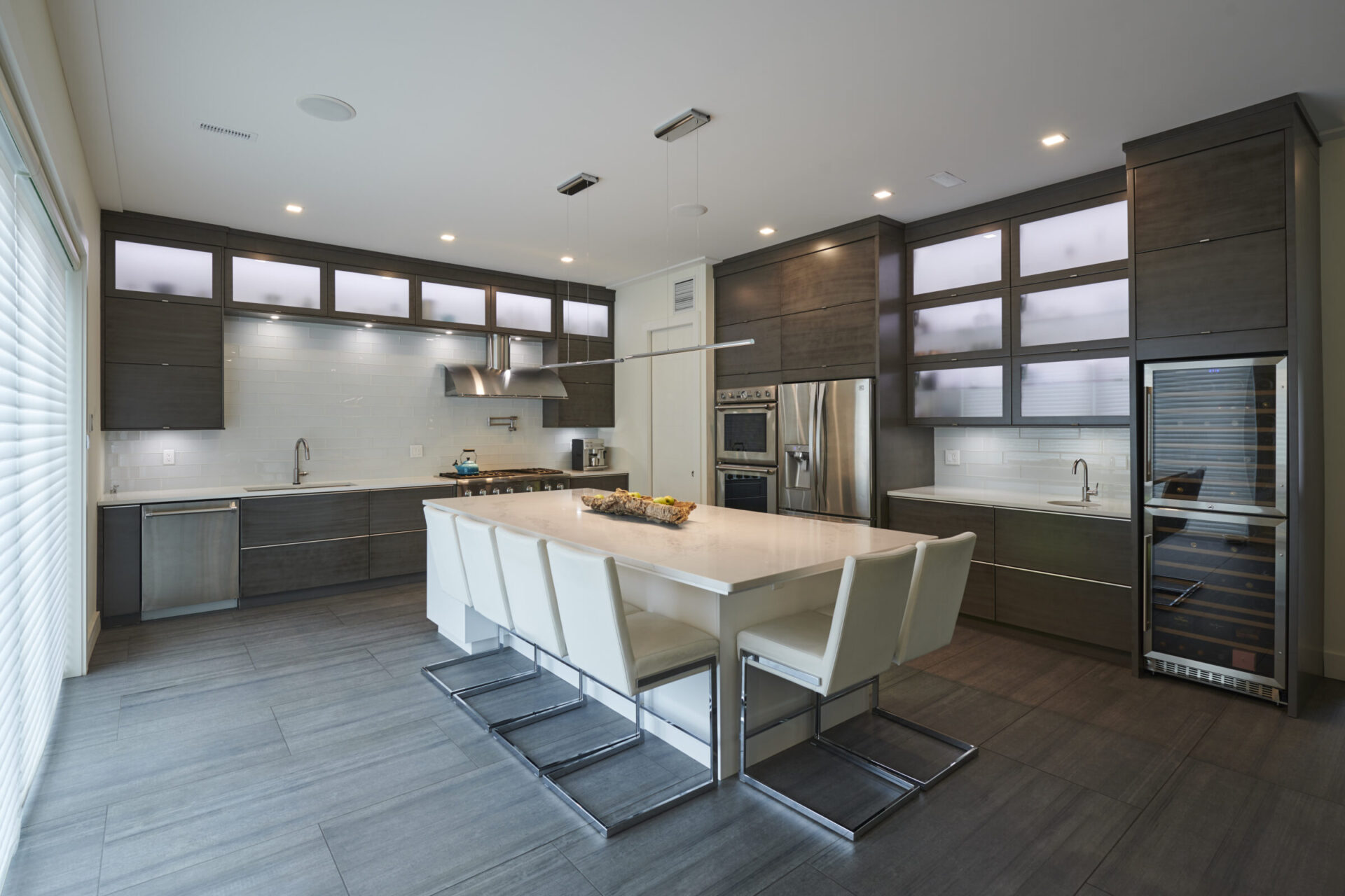 A modern kitchen with dark wood cabinets, stainless steel appliances, a white countertop island with seating, and a wine fridge. Elegant and spacious design.