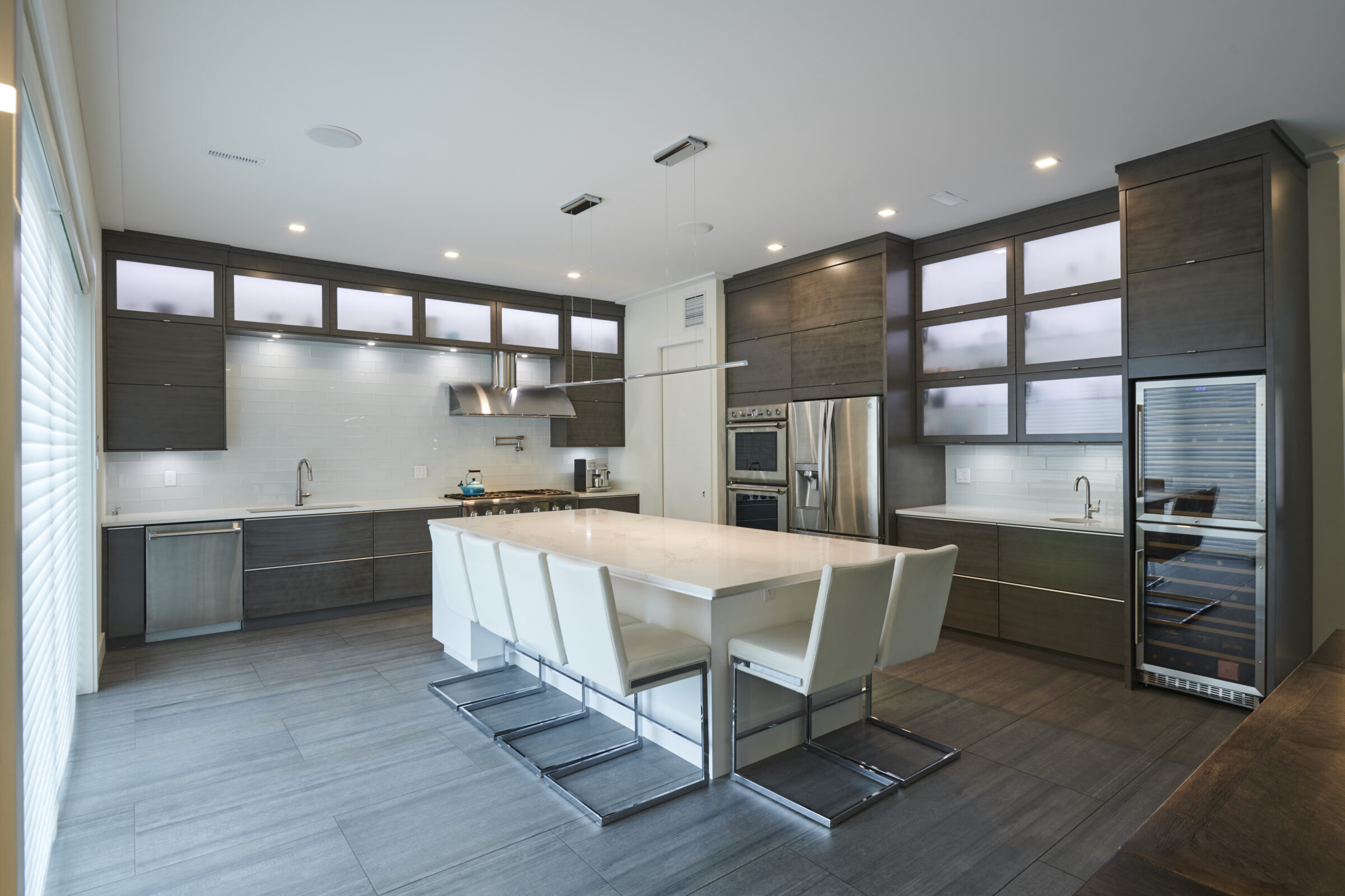 Modern kitchen with gray wooden cabinets, stainless steel appliances, a large white island with seating, tiled backsplash, and pendant lighting fixtures.