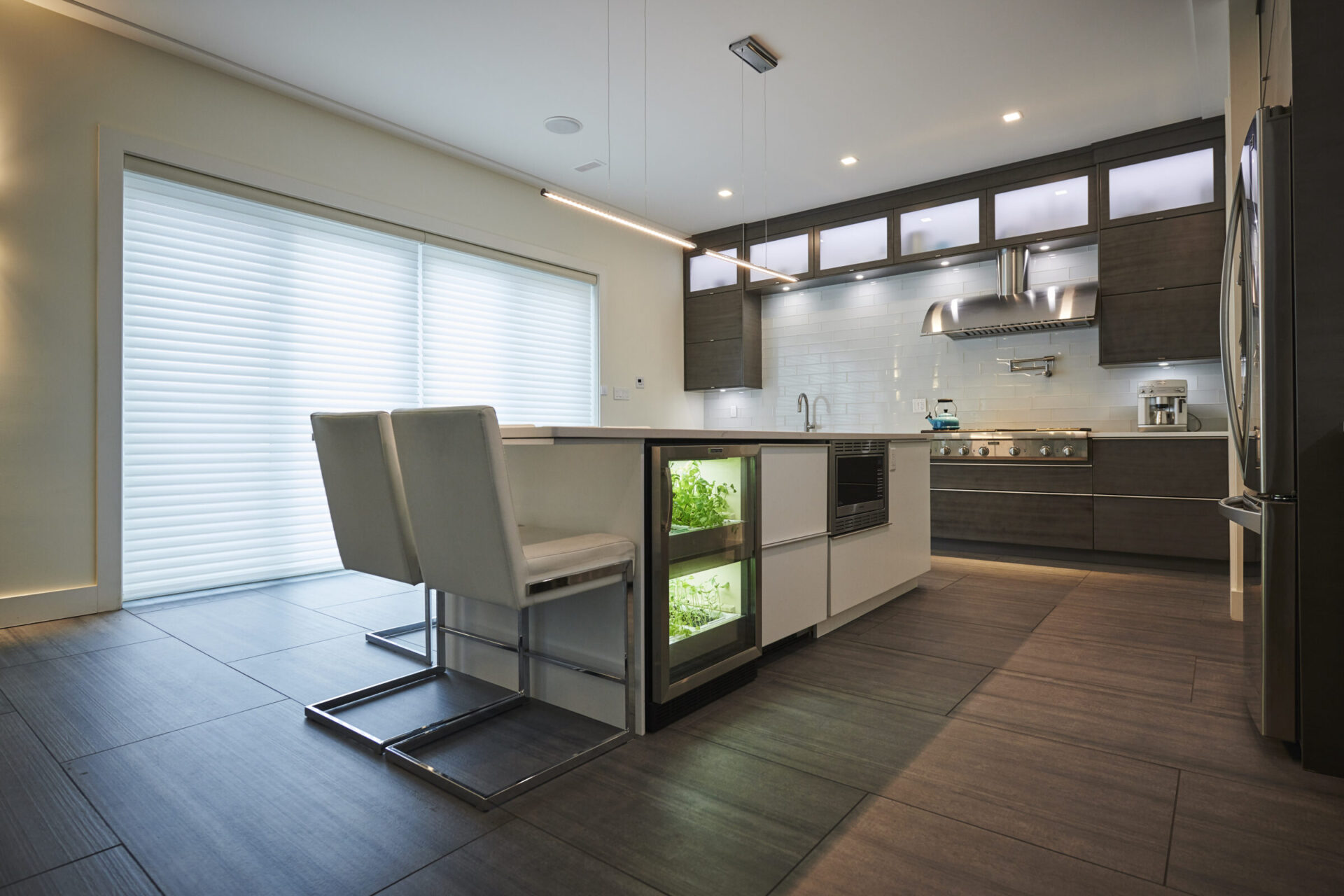 A modern kitchen with dark cabinetry, integrated appliances, an under-cabinet lighting system, a dining area, and an indoor plant cultivation cabinet.