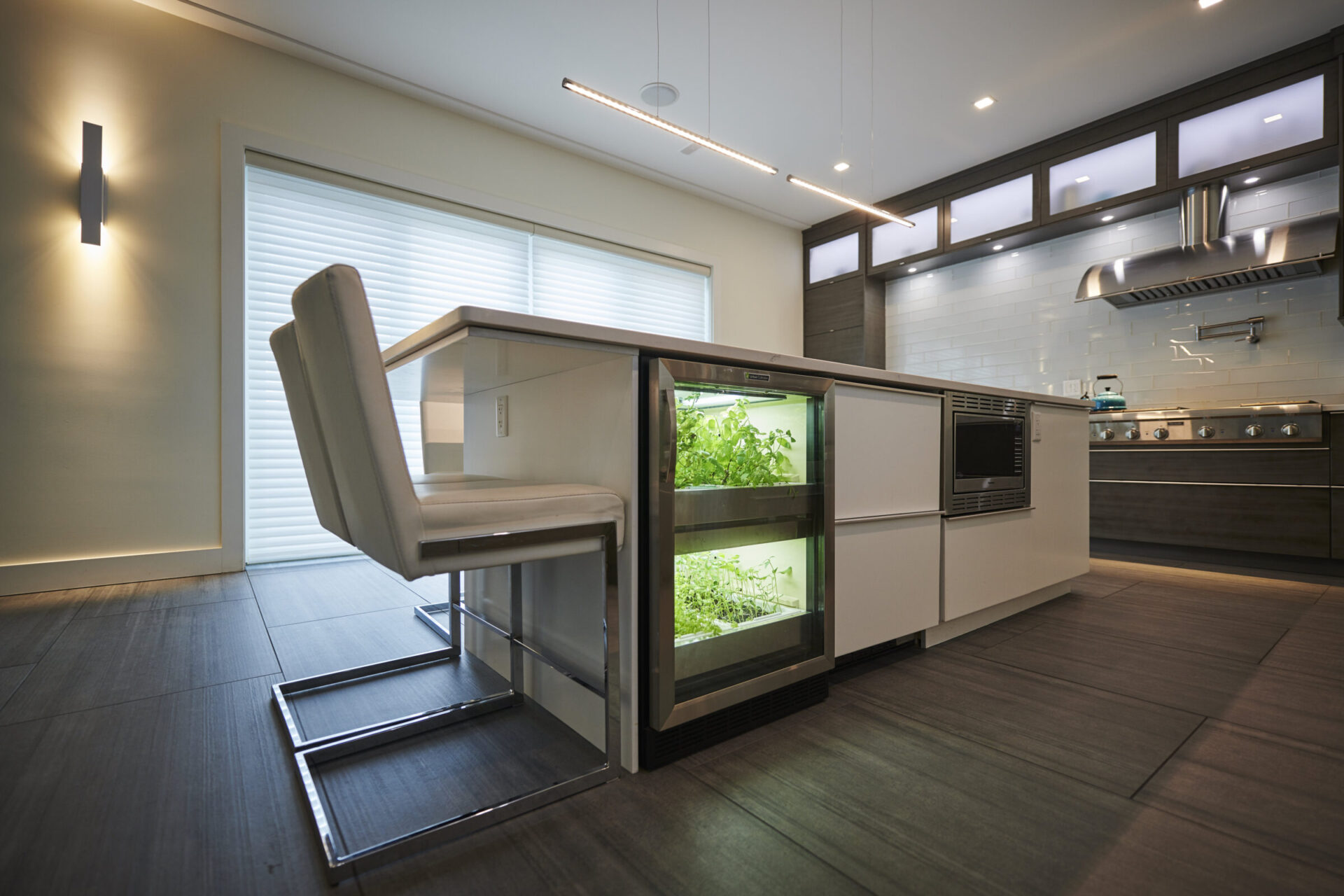A modern kitchen with LED lighting, sleek cabinetry, and an indoor herb garden cabinet next to a high chair at a breakfast bar.