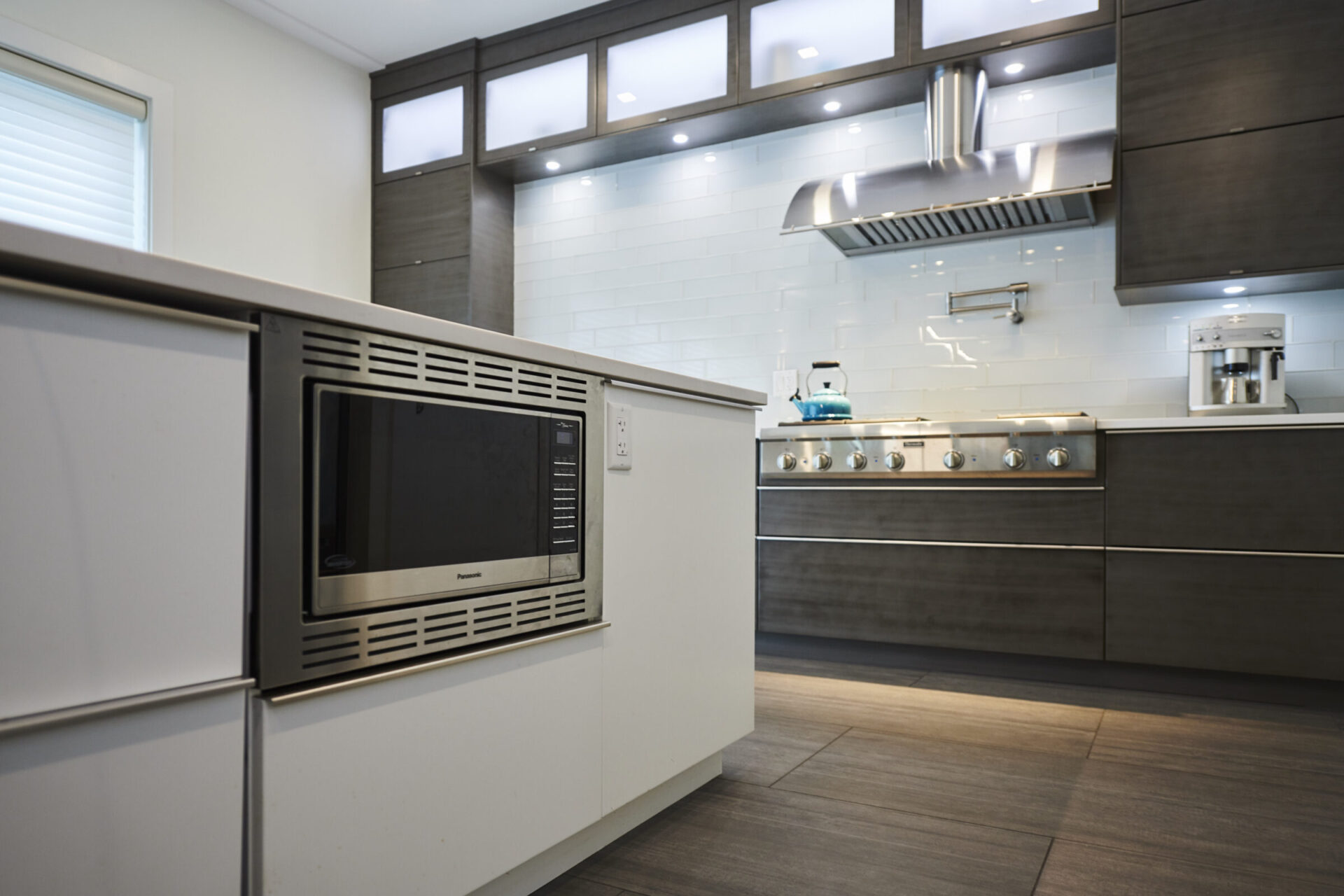 Modern kitchen with stainless steel appliances, dark wooden cabinets, white subway tiles, and a range hood over a stove, featuring a clean design.
