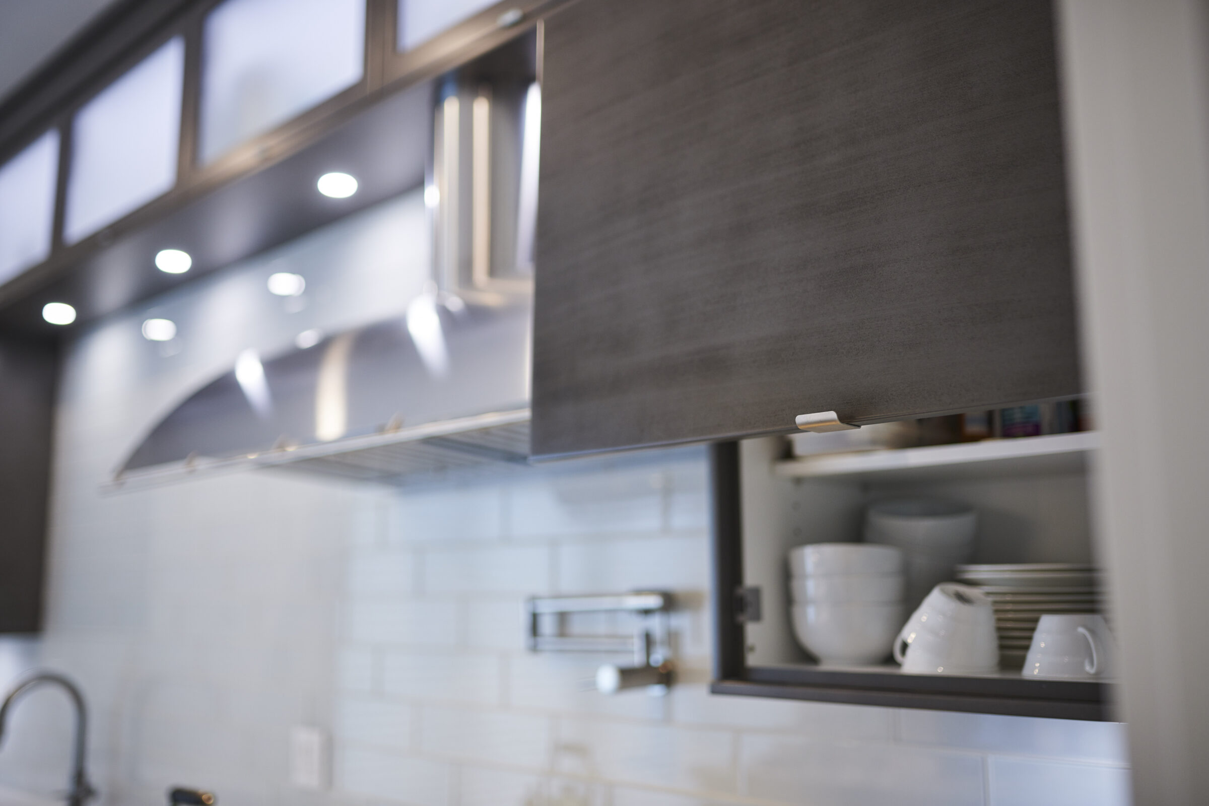 Modern kitchen interior with an open cabinet displaying neatly stacked white dishes, under subtle lighting, with a blurred background enhancing the focus.