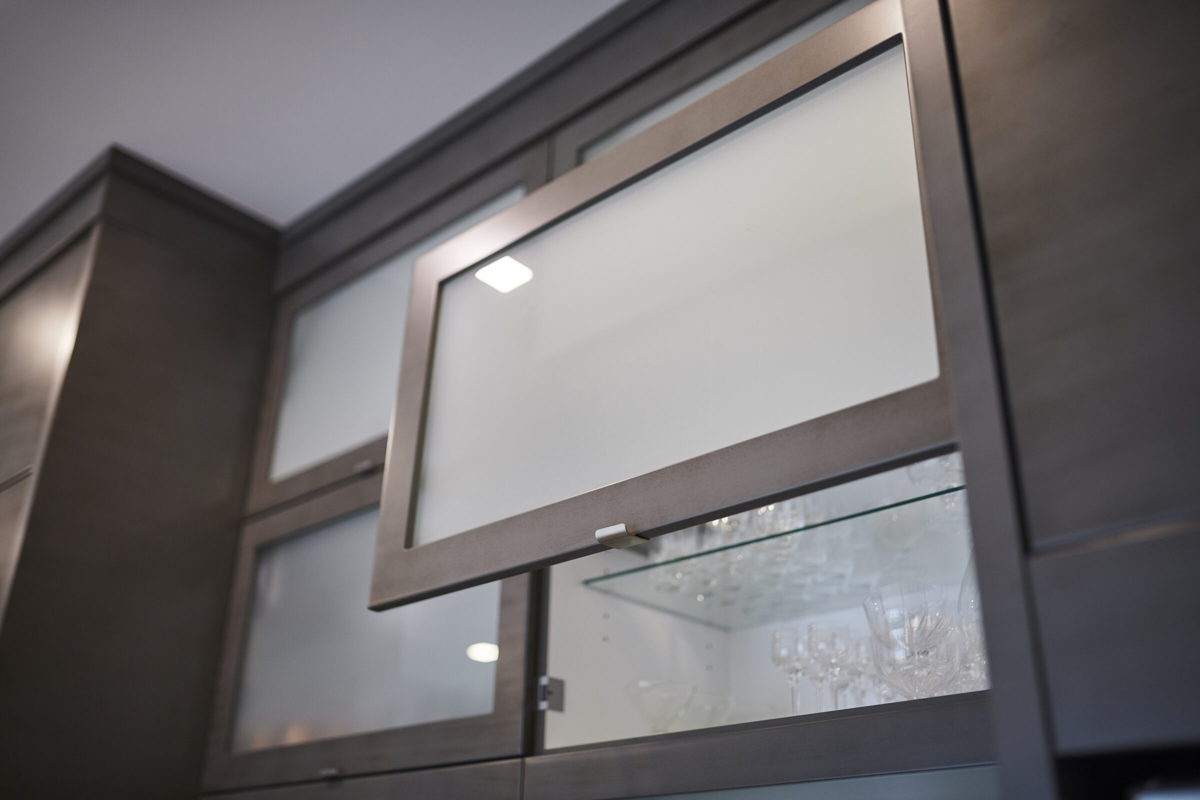 Modern kitchen cabinet with frosted glass and LED lighting, displaying clear glassware inside. Neutral colors and a sleek design create an elegant atmosphere.