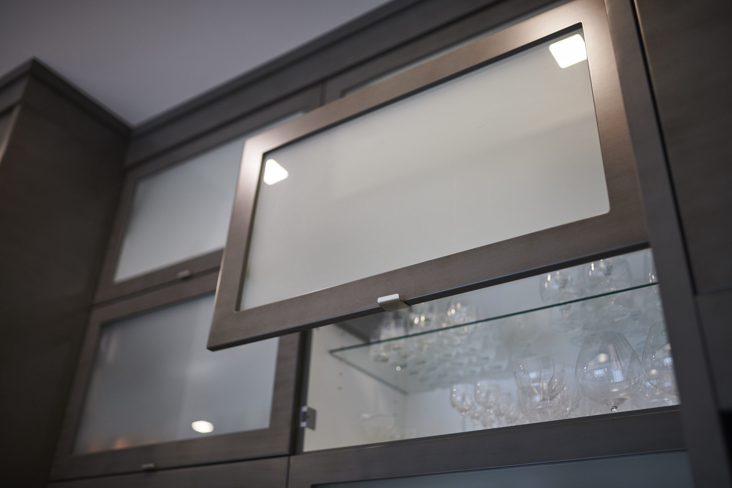 A modern kitchen cabinet with frosted glass and built-in lighting, holding clear glassware, exhibiting a sleek design in a contemporary home setting.