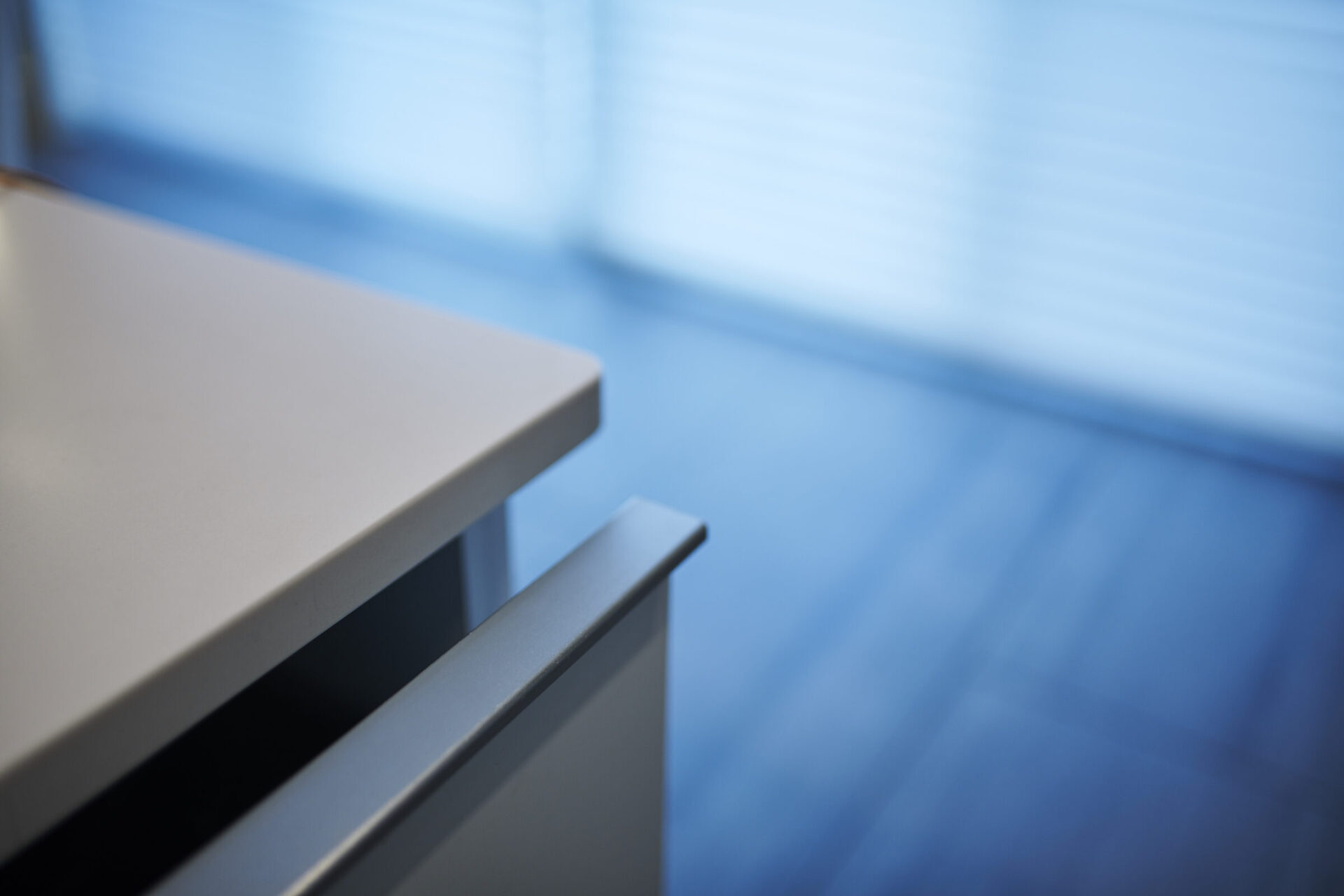 A close-up, blurred photo of an opened drawer in a minimalistic setting with a white counter and blue-tinted background, likely indicating a modern interior design.