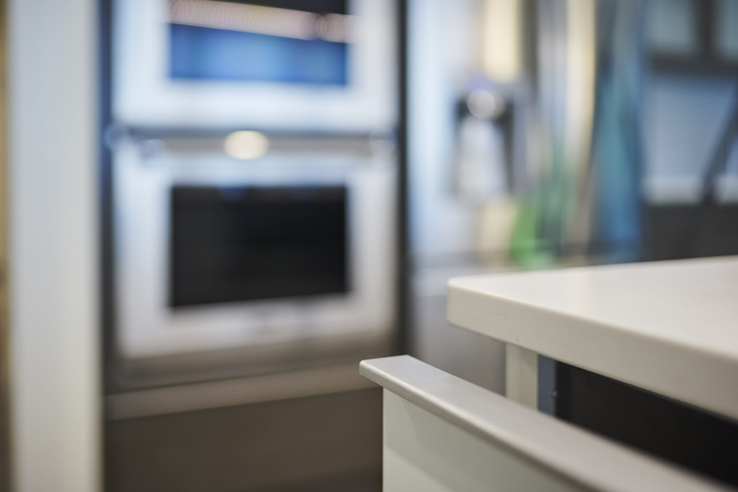 This is a blurred kitchen interior focusing on a countertop edge, with an oven in the background and a glimpse of cabinet handles and kitchenware.