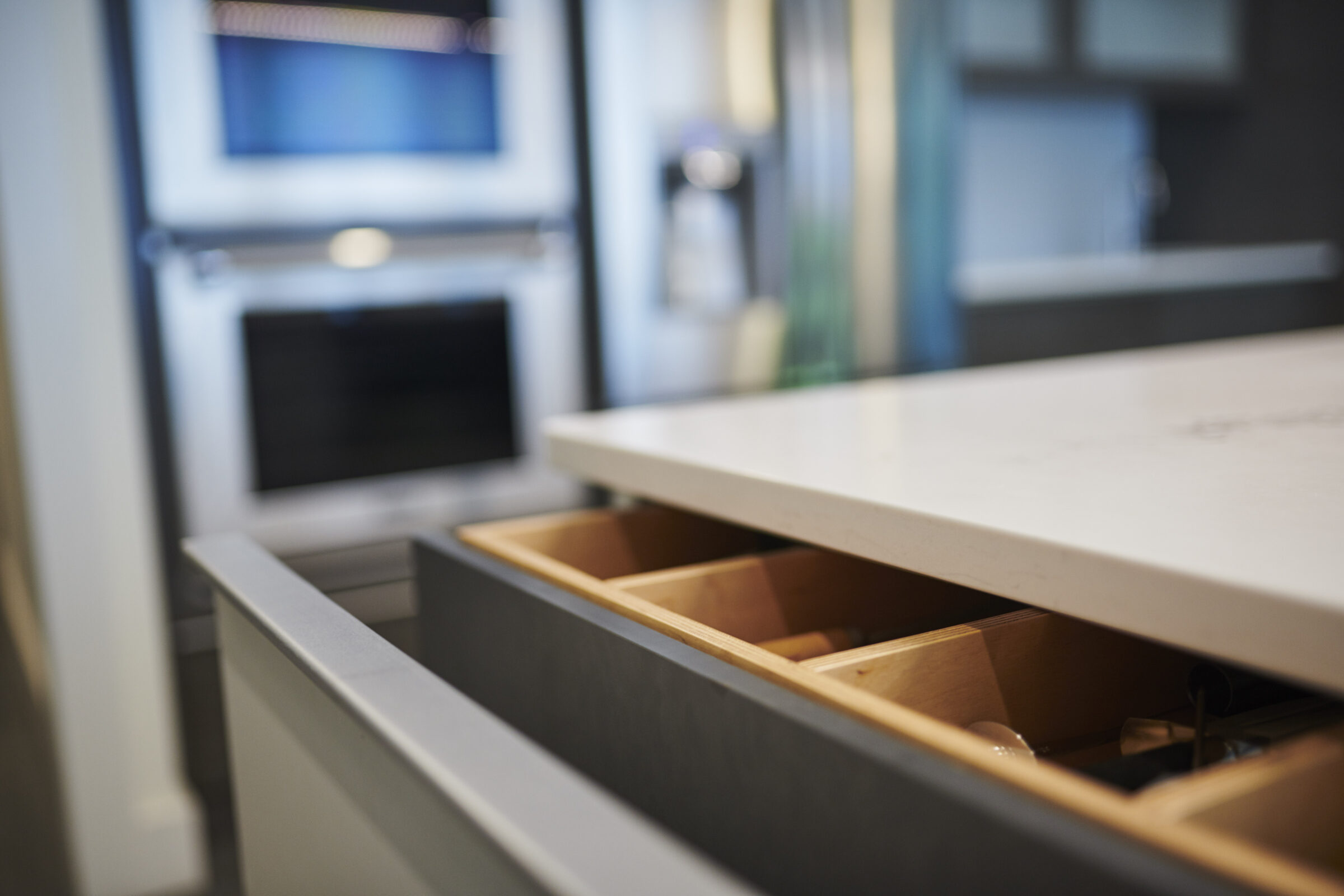 This is a close-up image of an open drawer in a modern kitchen, with a blurred background showing a countertop and appliances.