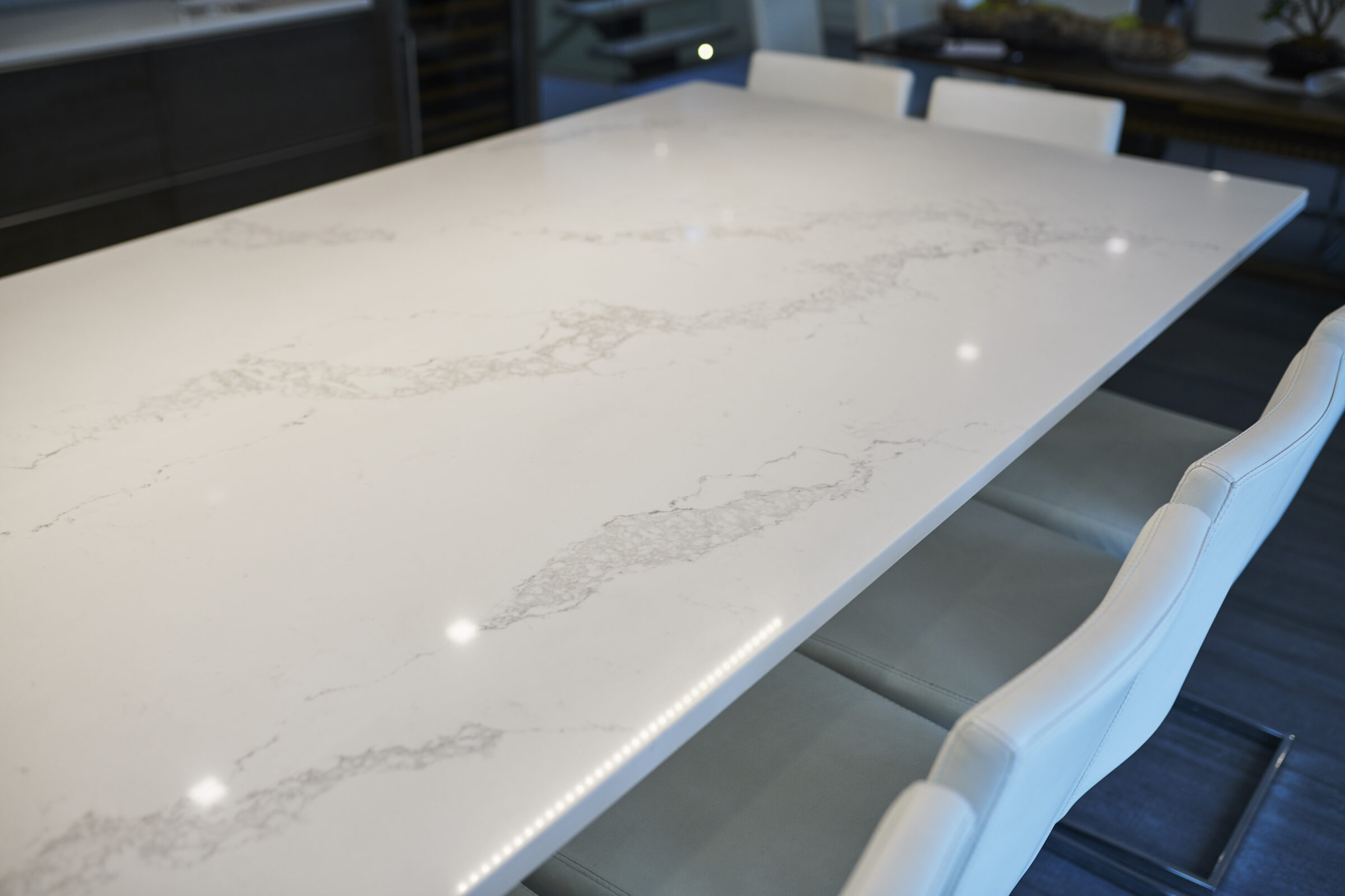 Modern interior with a large white marble-topped table and sleek white chairs. Reflective surfaces and soft lighting create an elegant atmosphere.