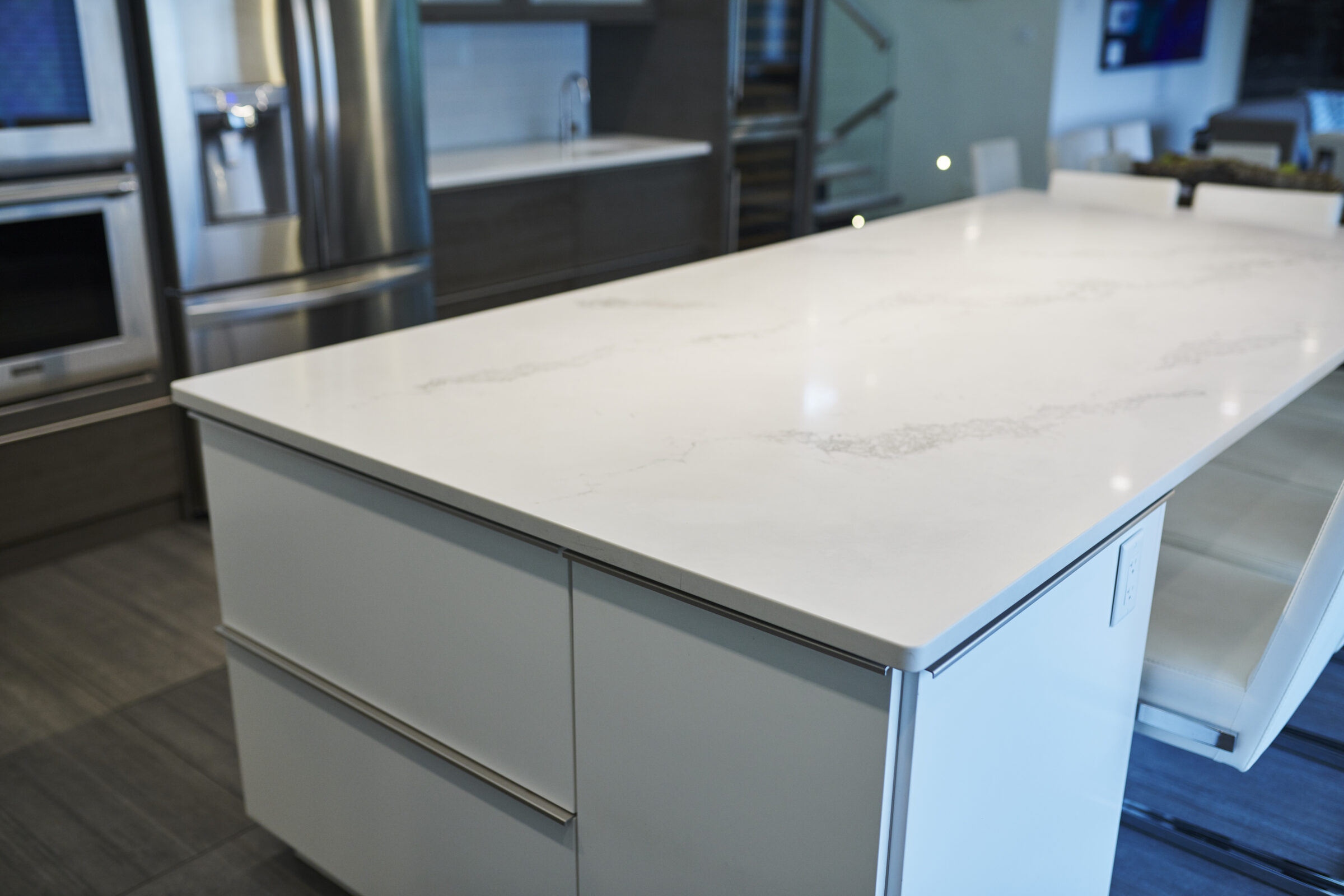 This is a modern kitchen with a large marble countertop island, stainless steel appliances, grey cabinetry, and ambient lighting.