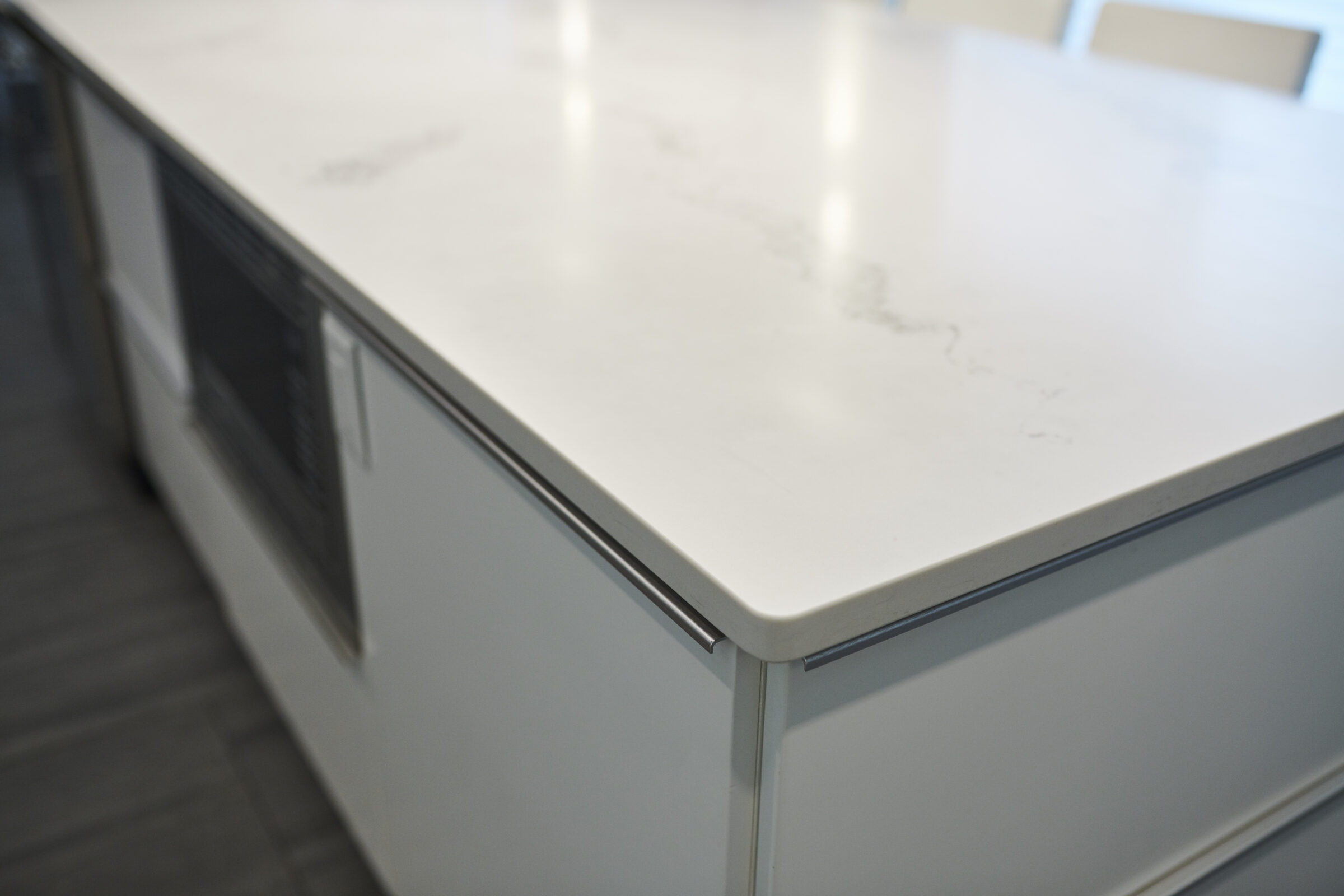 This image features a close-up of a white, marble-patterned countertop with the edge of a built-in kitchen cabinet or appliance visible.