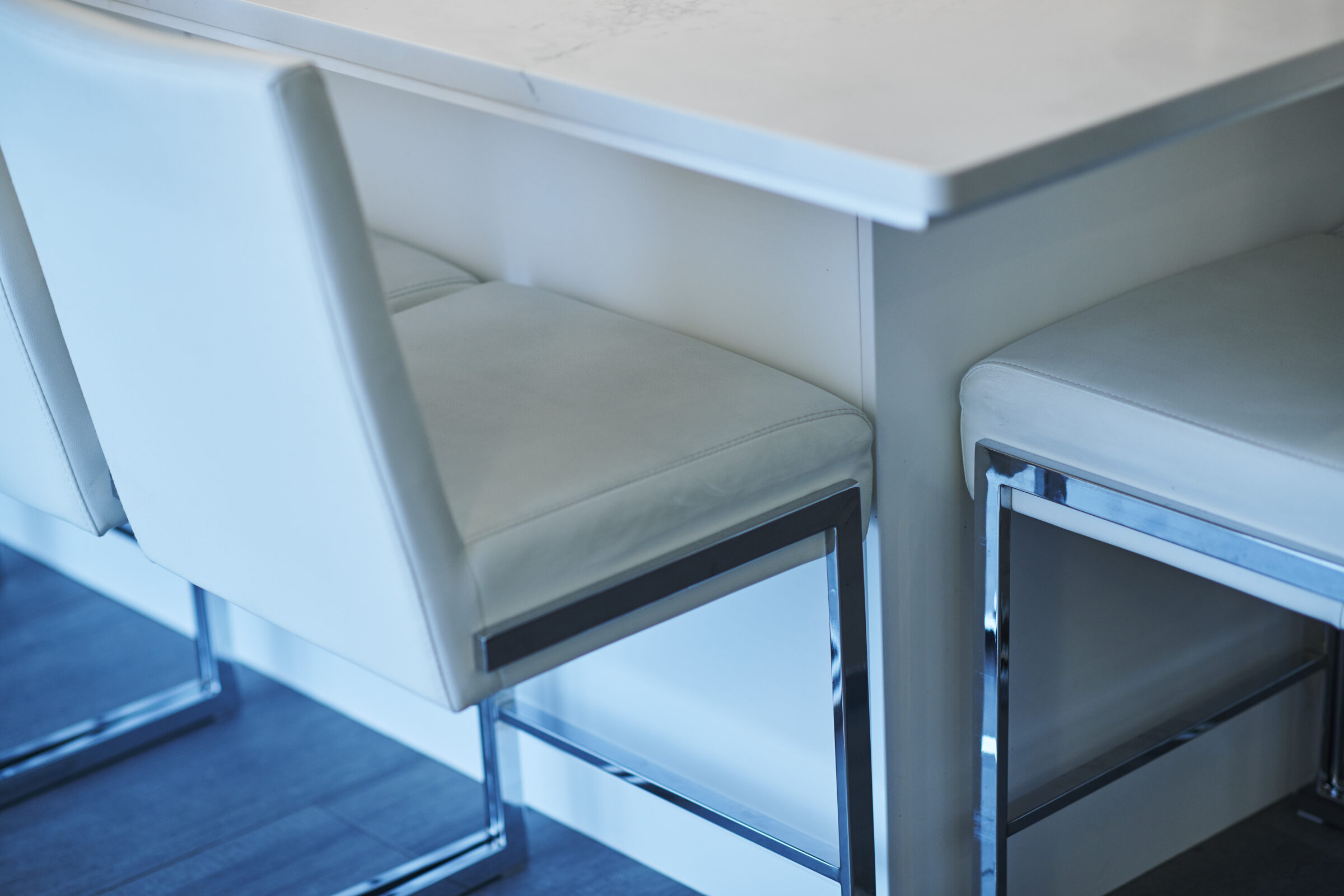 A modern dining area with a white marble table and two leather chairs featuring metal legs, set in a room with soft natural lighting.