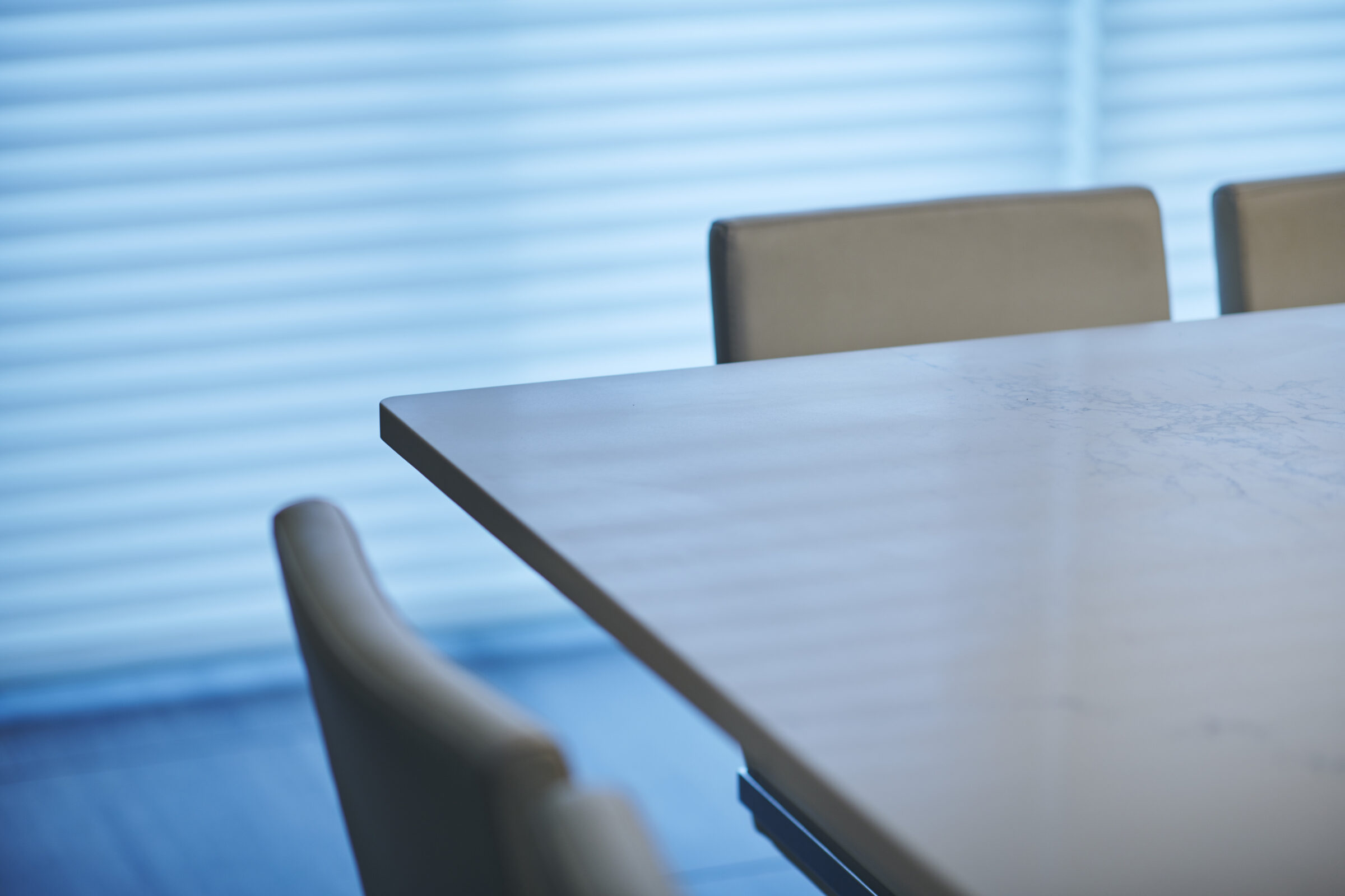 A modern conference room with a sleek table, comfortable chairs, and striped window blinds casting soft light across the serene setting.