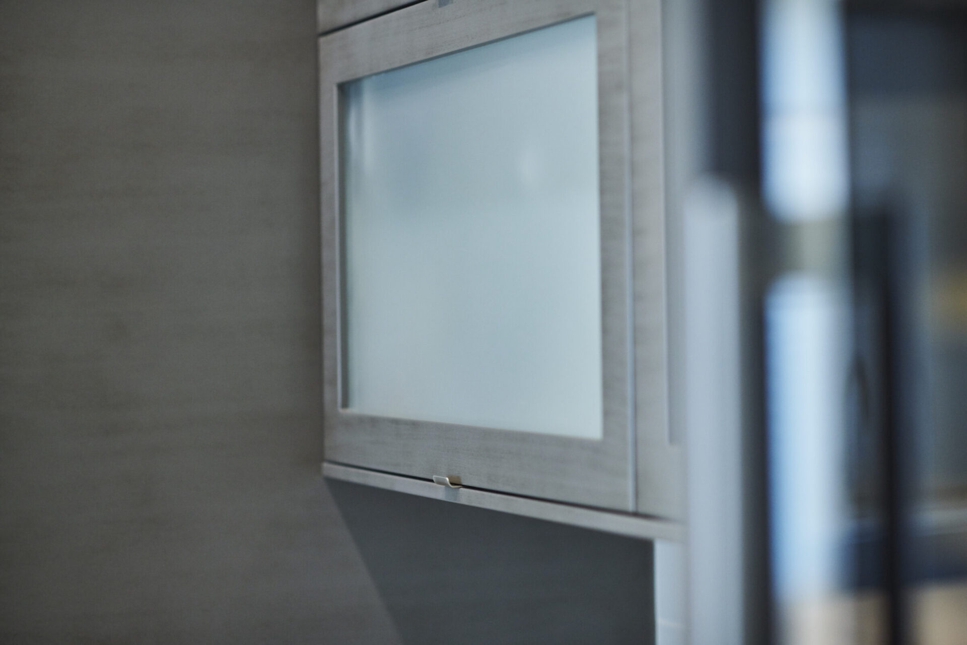 This image features a close-up view of a frosted glass cabinet door with a metal handle, set against a blurred interior background.