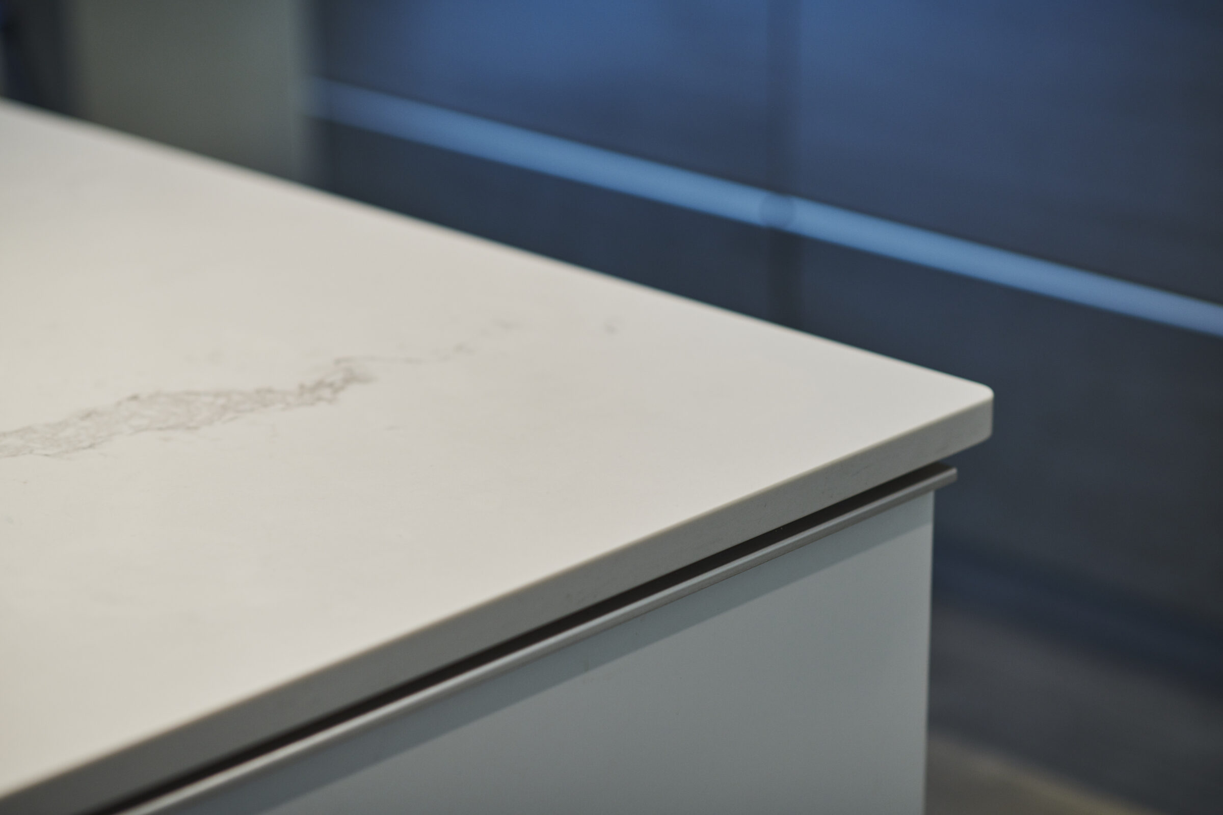 This image shows a close-up of a white countertop with a visible stain, above a white drawer with a silver handle, against a blue background.