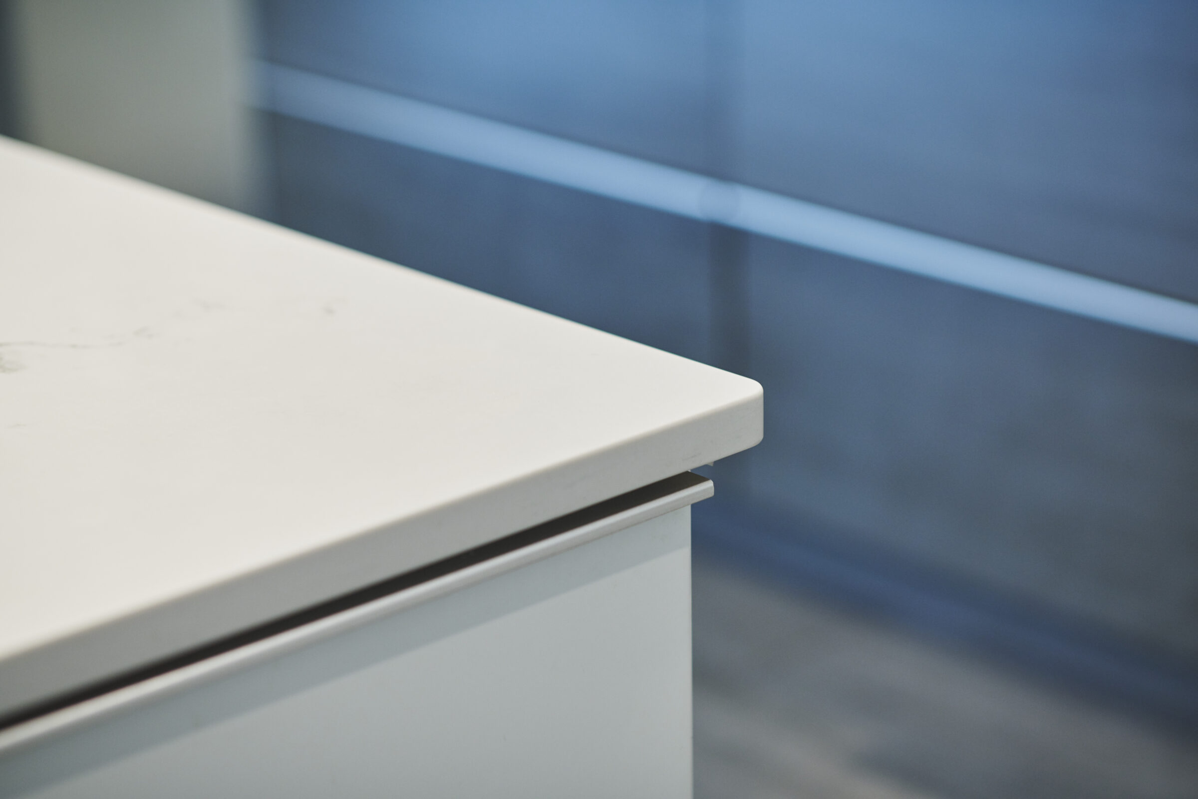 An image featuring a close-up of a white tabletop with a focus on the edge, against a blurred blue and gray background. No people are present.