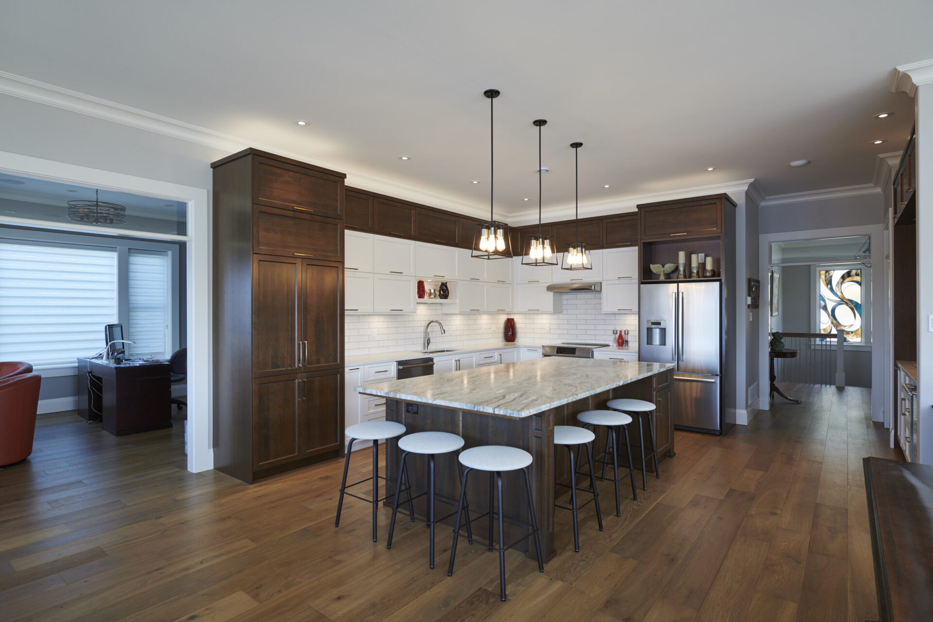This image shows a spacious kitchen with white cabinets, dark wood furniture, stainless steel appliances, bar stools, and pendant lighting.