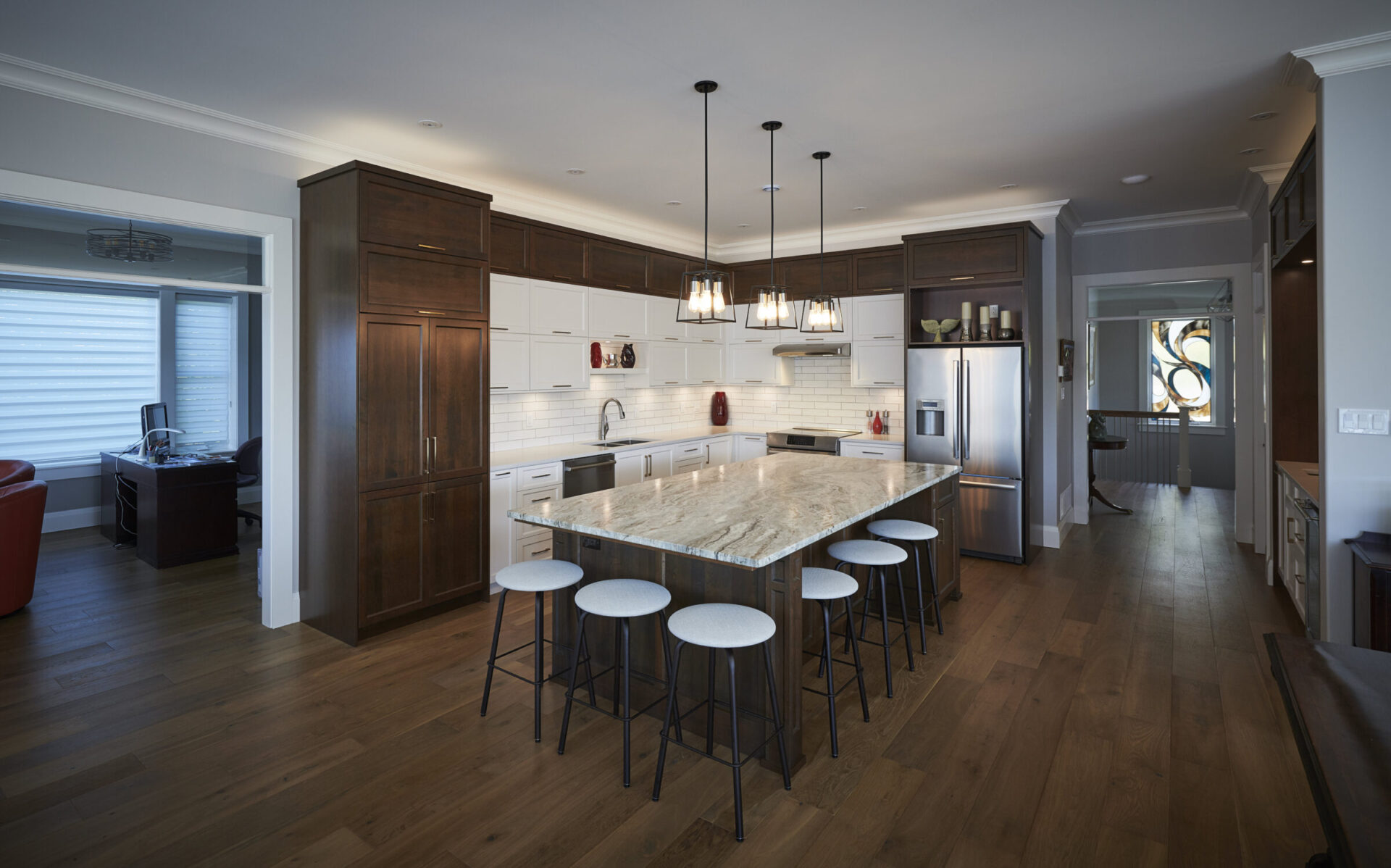 The image shows a modern kitchen with dark wood cabinets, white countertops, stainless steel appliances, an island with bar stools, and pendant lighting.