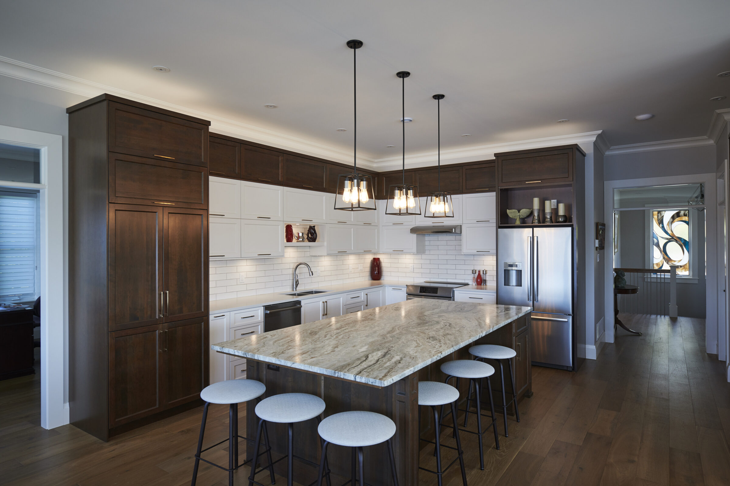 A modern kitchen with dark cabinets, white subway tile backsplash, stainless steel appliances, a large island with stools, and pendant lighting.