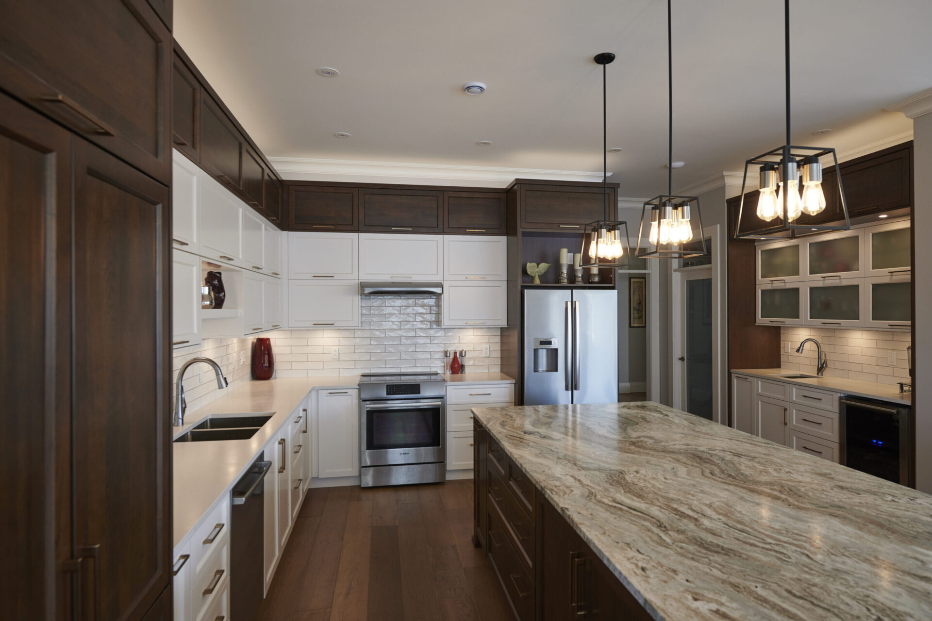 Modern kitchen interior with white cabinetry, dark wood accents, stainless steel appliances, marble countertops, and elegant pendant lighting. Clean and spacious design.
